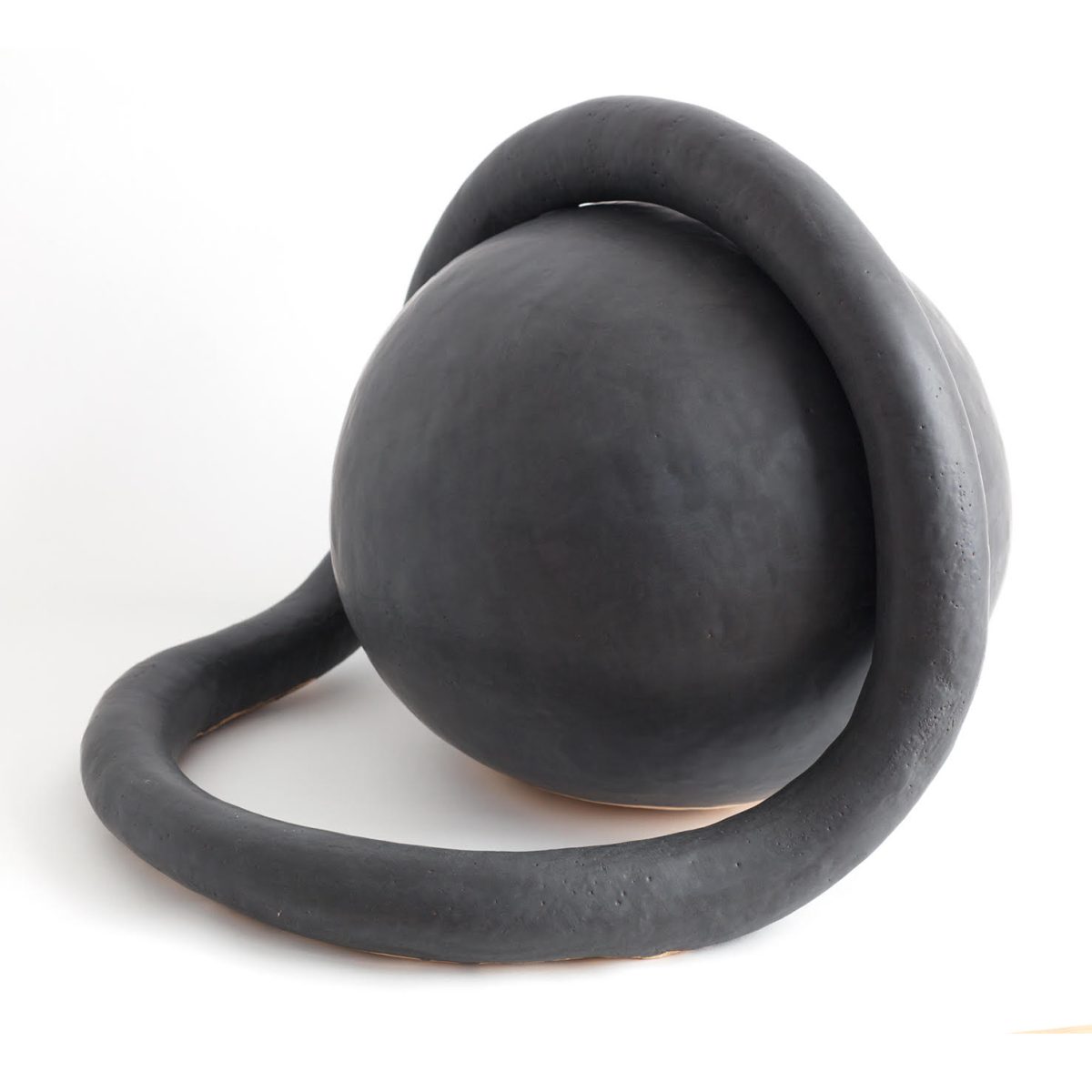 Abstract ceramic sculpture in dark charcoal glaze featuring a curved, organic form with a spherical element perched atop a sweeping, loop-like base, set against a white background.