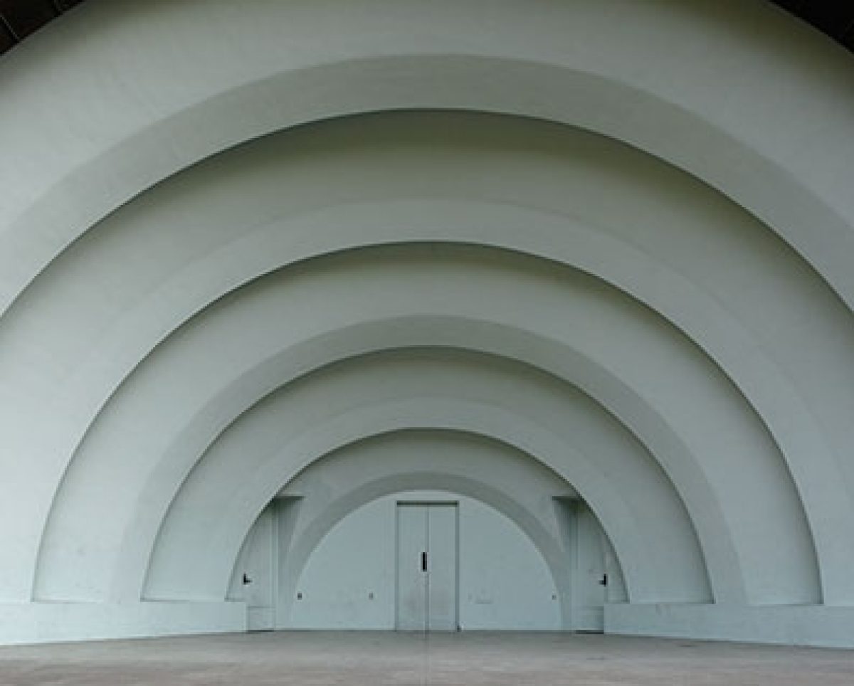 A series of concentric white arched structures recede toward a distant doorway in the center, creating a tunnel-like perspective. The geometric composition emphasizes depth and symmetry through repeated curved architectural forms against a minimal, monochromatic interior space.