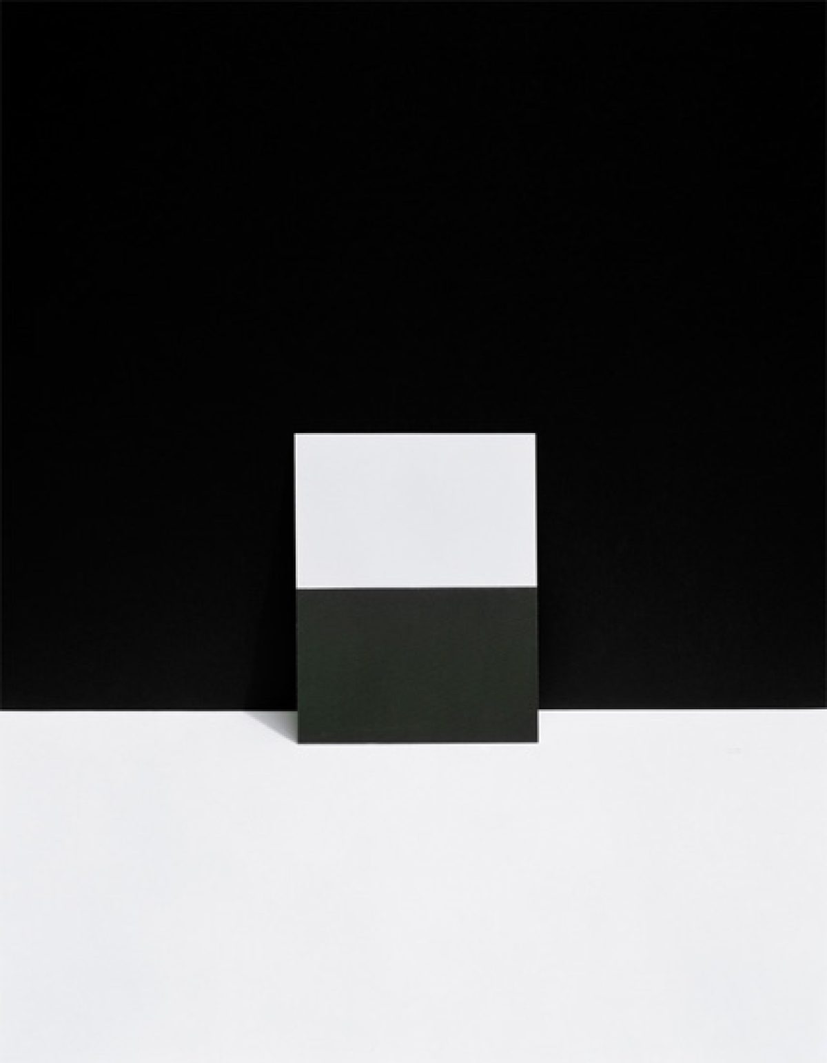 A geometric composition divided by a dark horizontal band, with a light gray rectangular form positioned above against a black background, and a lighter gray section below, creating a stark, minimalist arrangement of overlapping planes and tonal contrasts.