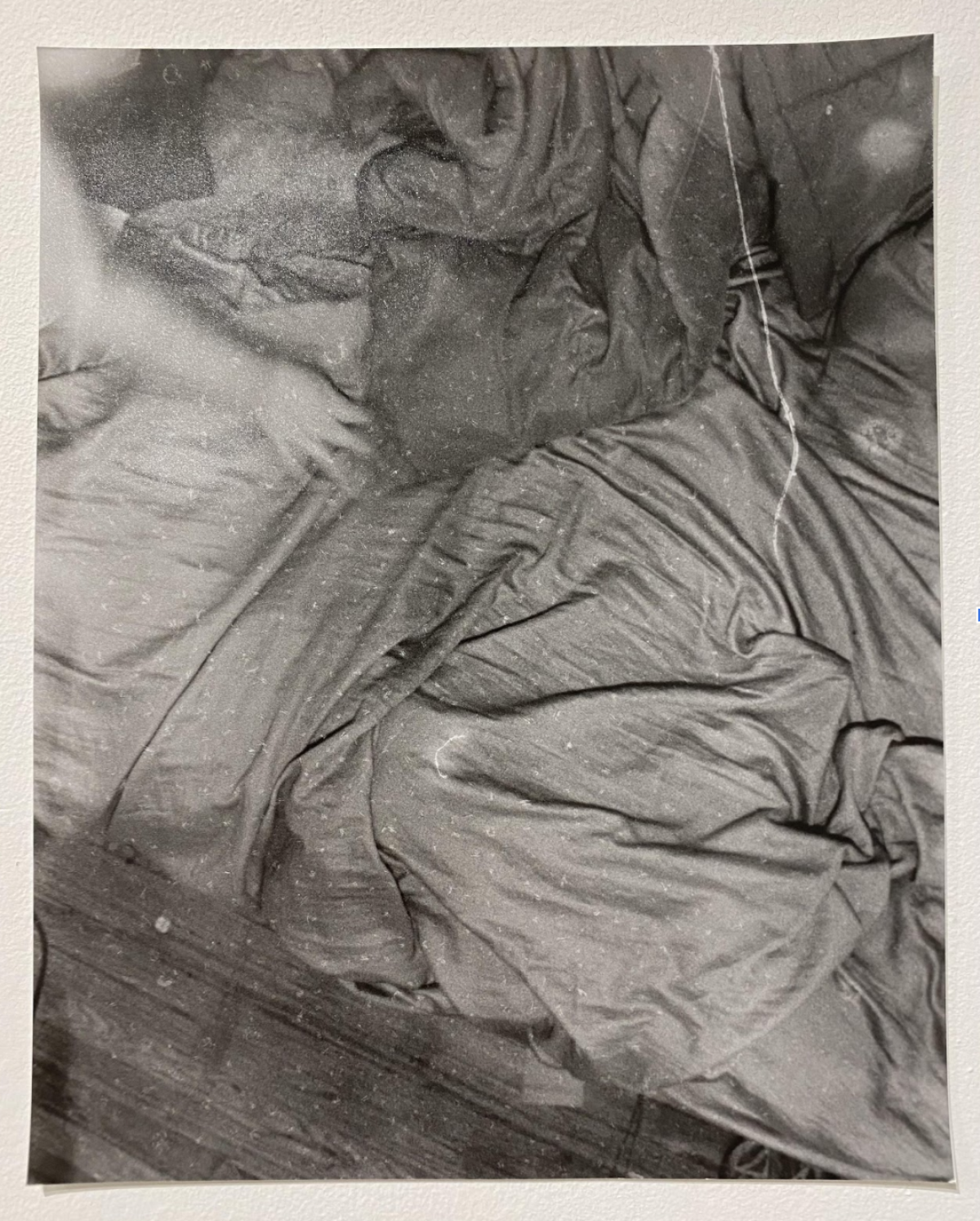 Black and white photograph of crumpled bedsheets and fabric, captured from above. The composition emphasizes the play of light and shadow across deep folds and wrinkles, creating an abstract study of texture and form in the tangled cloth.