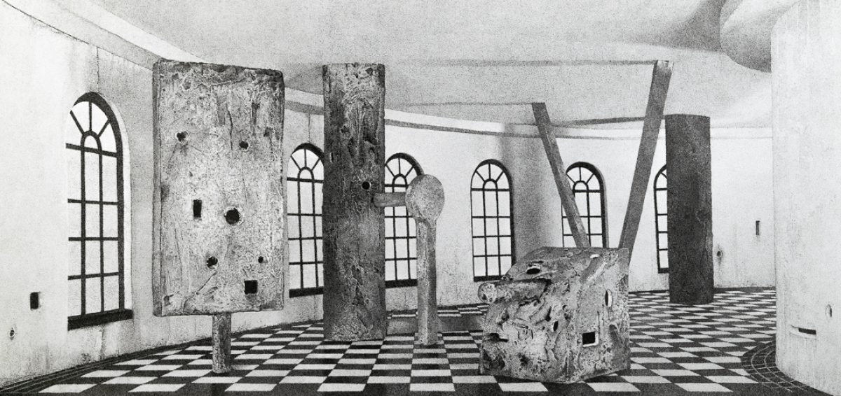 Black and white architectural interior with weathered concrete columns and walls featuring a geometric checkerboard floor. Multiple arched windows with grid patterns line the space, while irregular holes and openings punctuate the surfaces, creating an ambiguous sense of decay or deliberate abstraction.