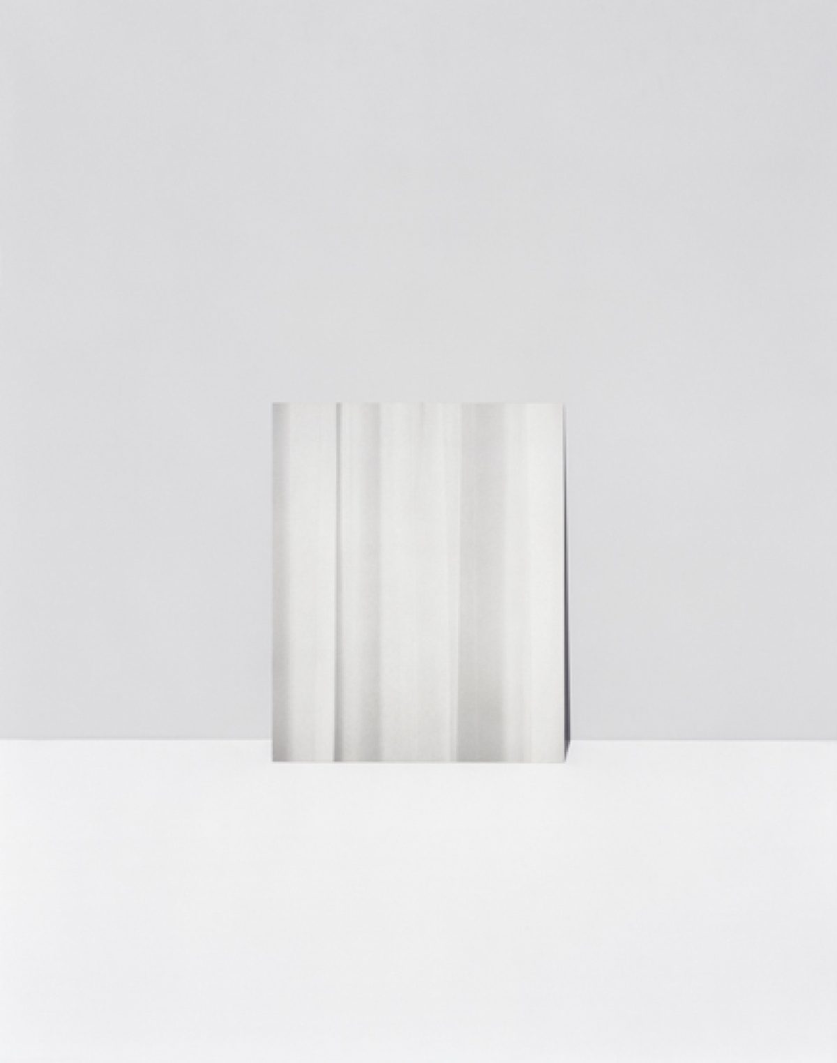 A minimalist composition featuring vertical folds or pleats of white and light gray material against a neutral gray background, creating subtle gradations of tone and shadow through gentle gradients and soft light.