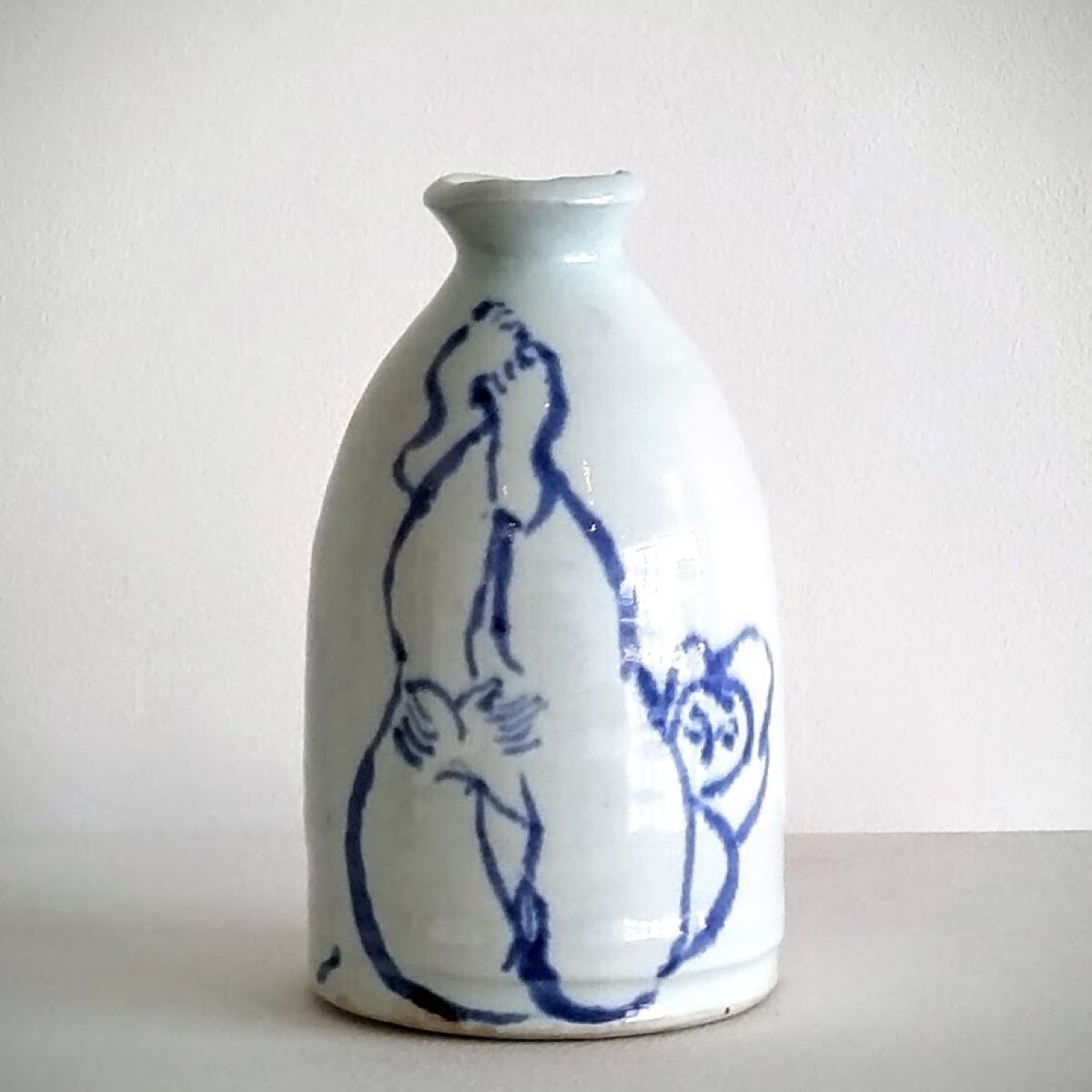 White porcelain bottle with a narrow neck and bulbous body, decorated with loose cobalt blue line drawings of abstracted human figures in dynamic poses across its surface.