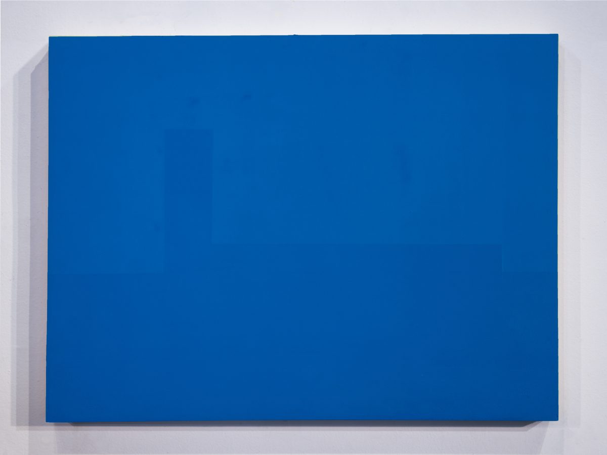 A vibrant blue rectangular panel mounted on a light gray wall, casting a subtle shadow. The monochromatic composition emphasizes the pure saturation of the blue pigment and the work's geometric minimalism.