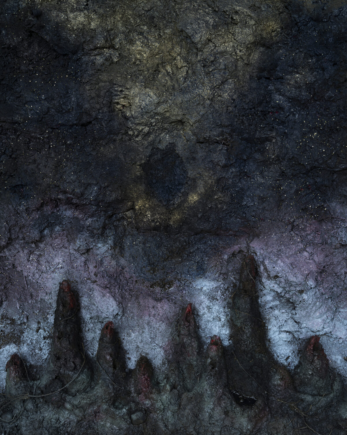 Textured photograph of a weathered stone surface with jagged, pointed formations rising from a pale, lichen-covered base, creating a dramatic contrast between dark rocky protrusions and lighter mineral deposits. Speckled highlights suggest starlight or crystalline particles across the eroded, monochromatic composition.