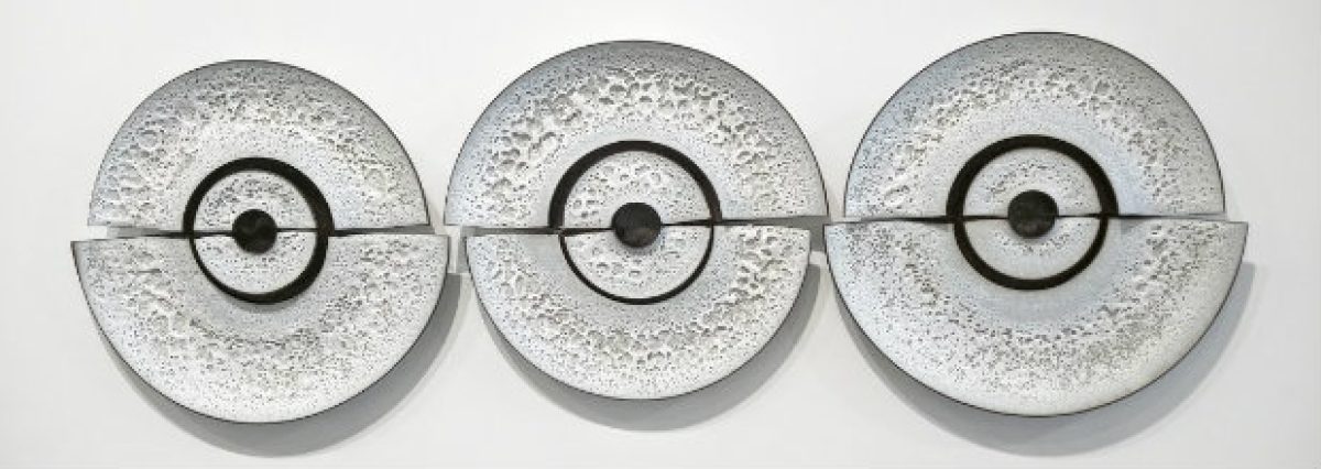 Three circular cast concrete or plaster discs arranged in a horizontal row, each featuring a textured surface with a central circular opening and concentric ring detail, creating a rhythmic, minimalist composition in monochromatic gray tones.