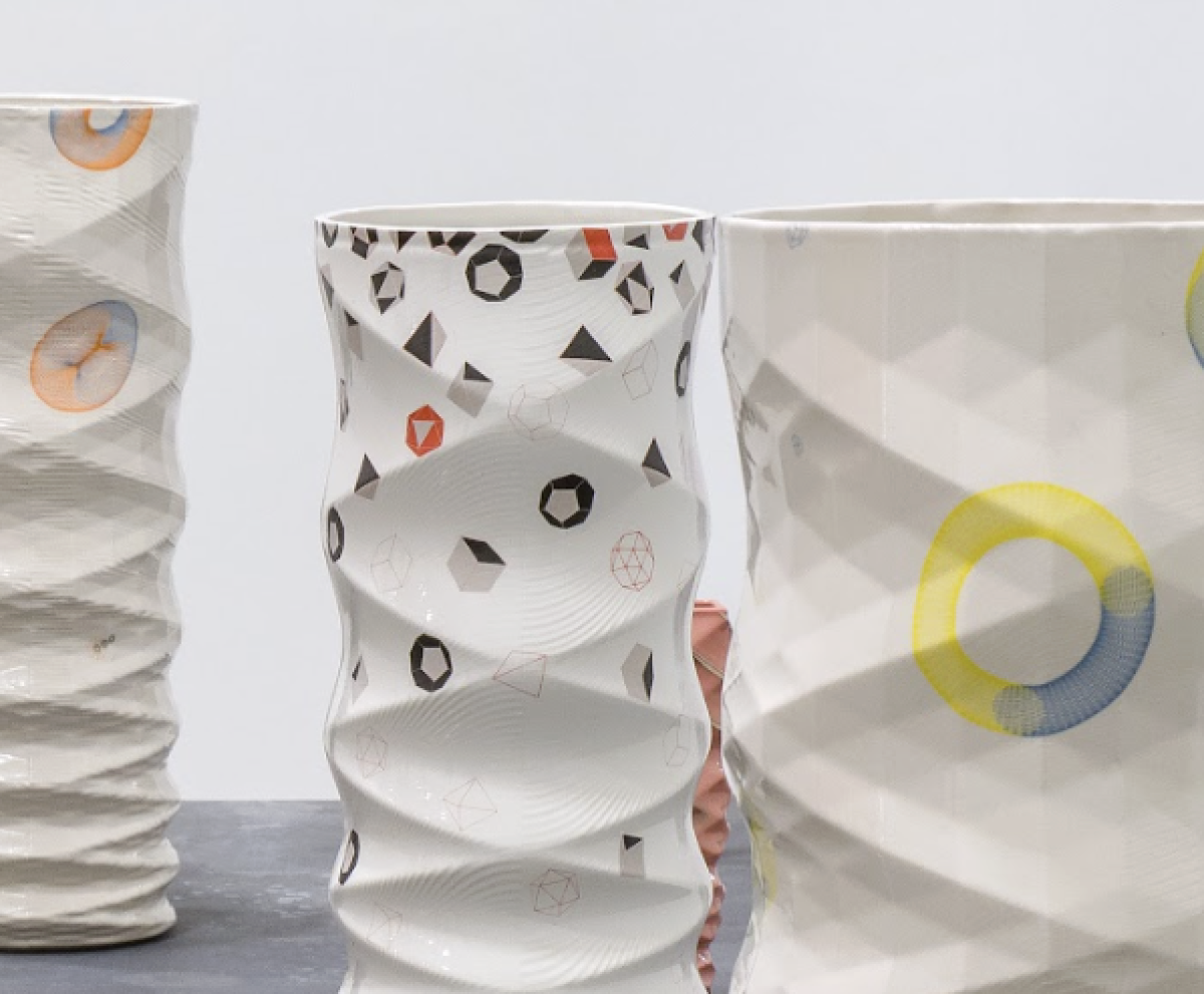 Three ceramic vessels with undulating white surfaces decorated with geometric patterns in black, red, and yellow. The forms feature wavy, rippled walls and circular graphic elements, displayed against a neutral background.