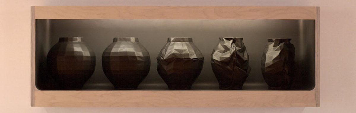 Five dark ceramic vessels arranged in a wooden shelf, progressing from rounded spherical forms on the left to increasingly angular and faceted shapes on the right, displayed against a neutral gray backdrop.