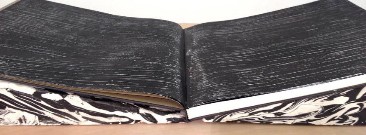 Open book with black linen covers and white and black marbled endpapers, surface densely marked with fine linear incisions and scratches creating an intricate pattern across the visible pages.