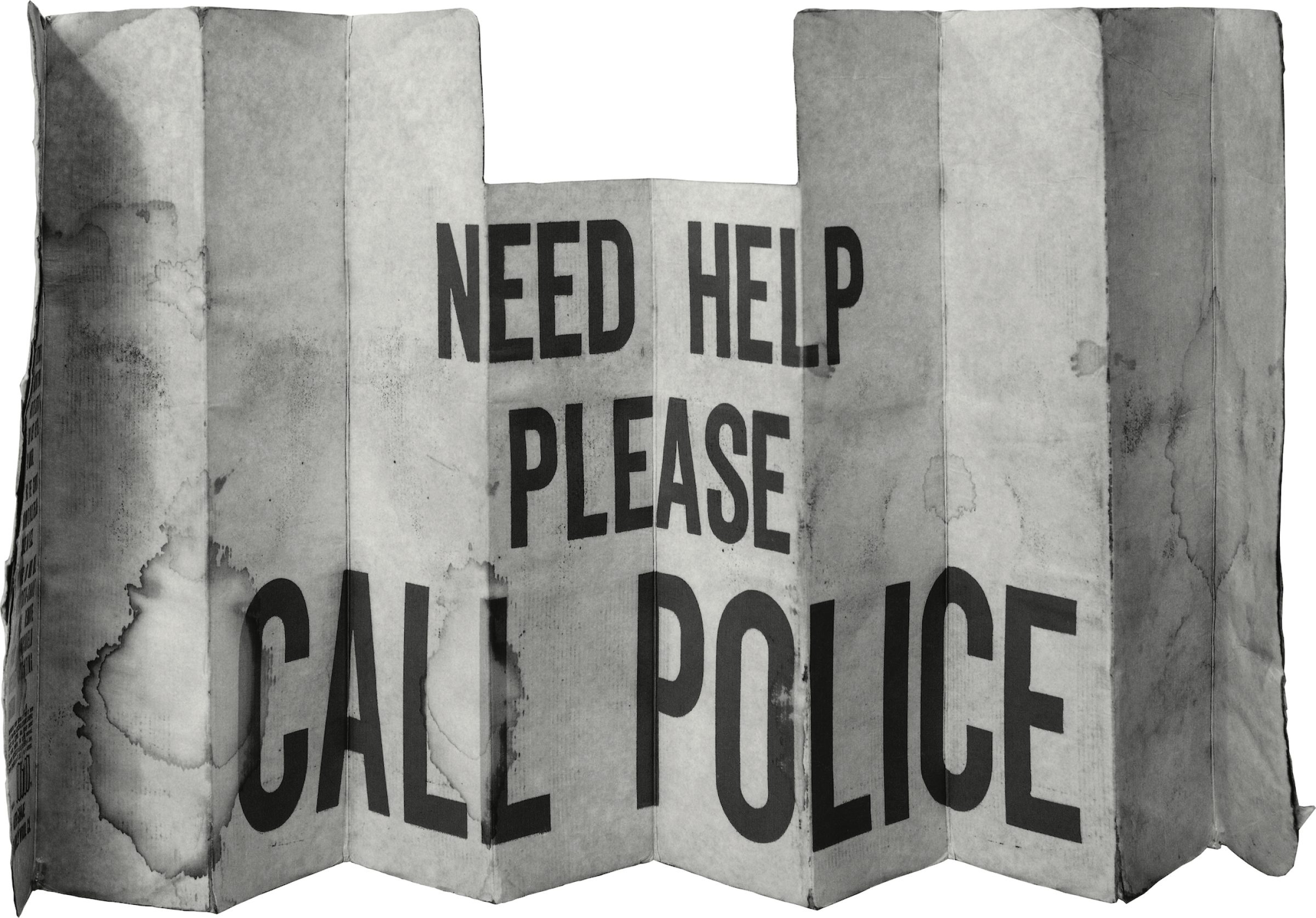 A weathered, accordion-folded metal panel resembling a car windshield sun shade, printed with bold black text reading "NEED HELP PLEASE CALL POLICE." The surface shows creasing, discoloration, and wear consistent with prolonged outdoor use.