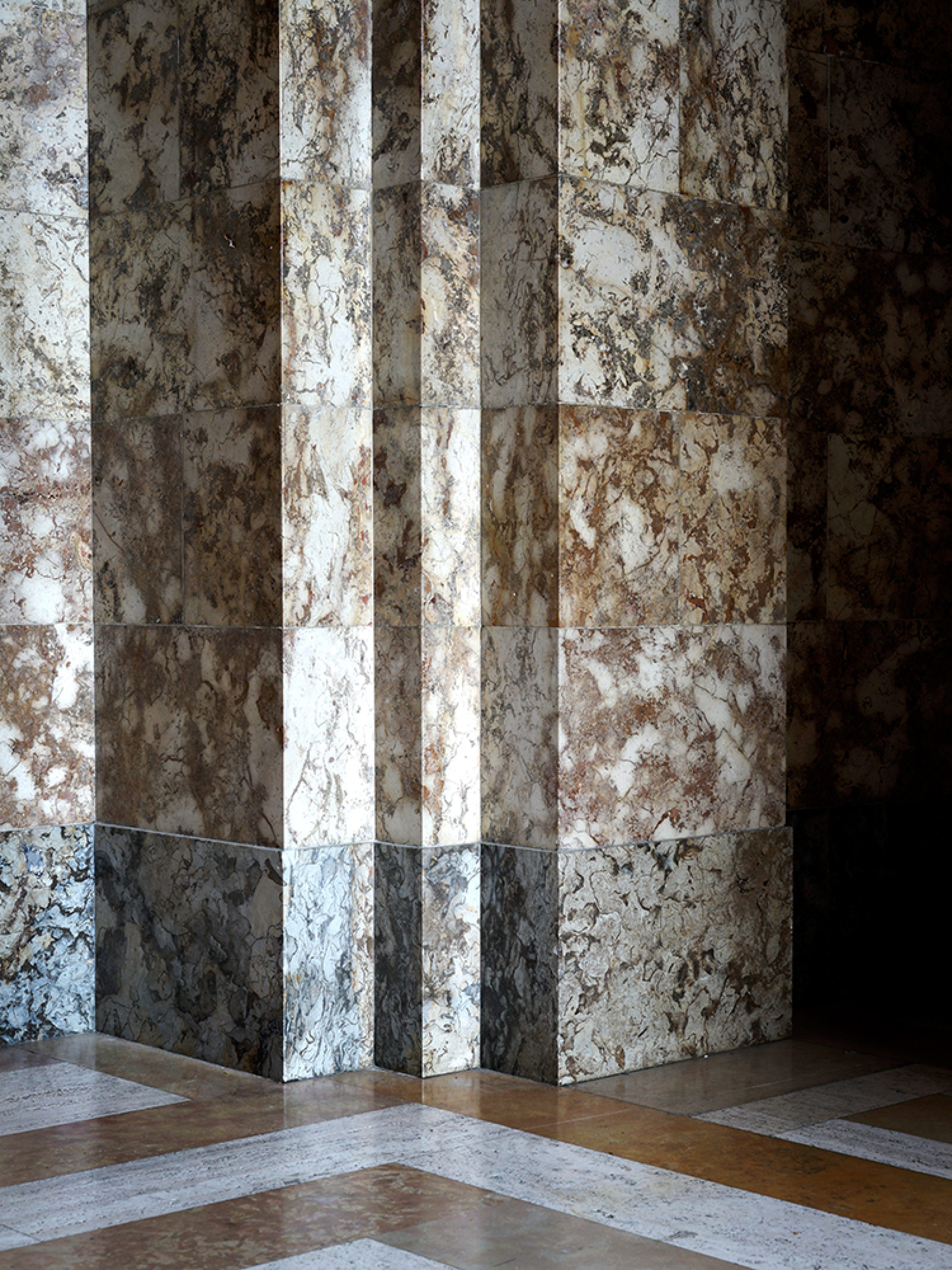 A corner view of a geometric interior featuring alternating vertical stripes of weathered white and dark surfaces, with distressed textures and rust-colored staining. The composition shows layered planes meeting at a right angle, with a polished floor in warm and cool tones reflecting the striped wall treatment.