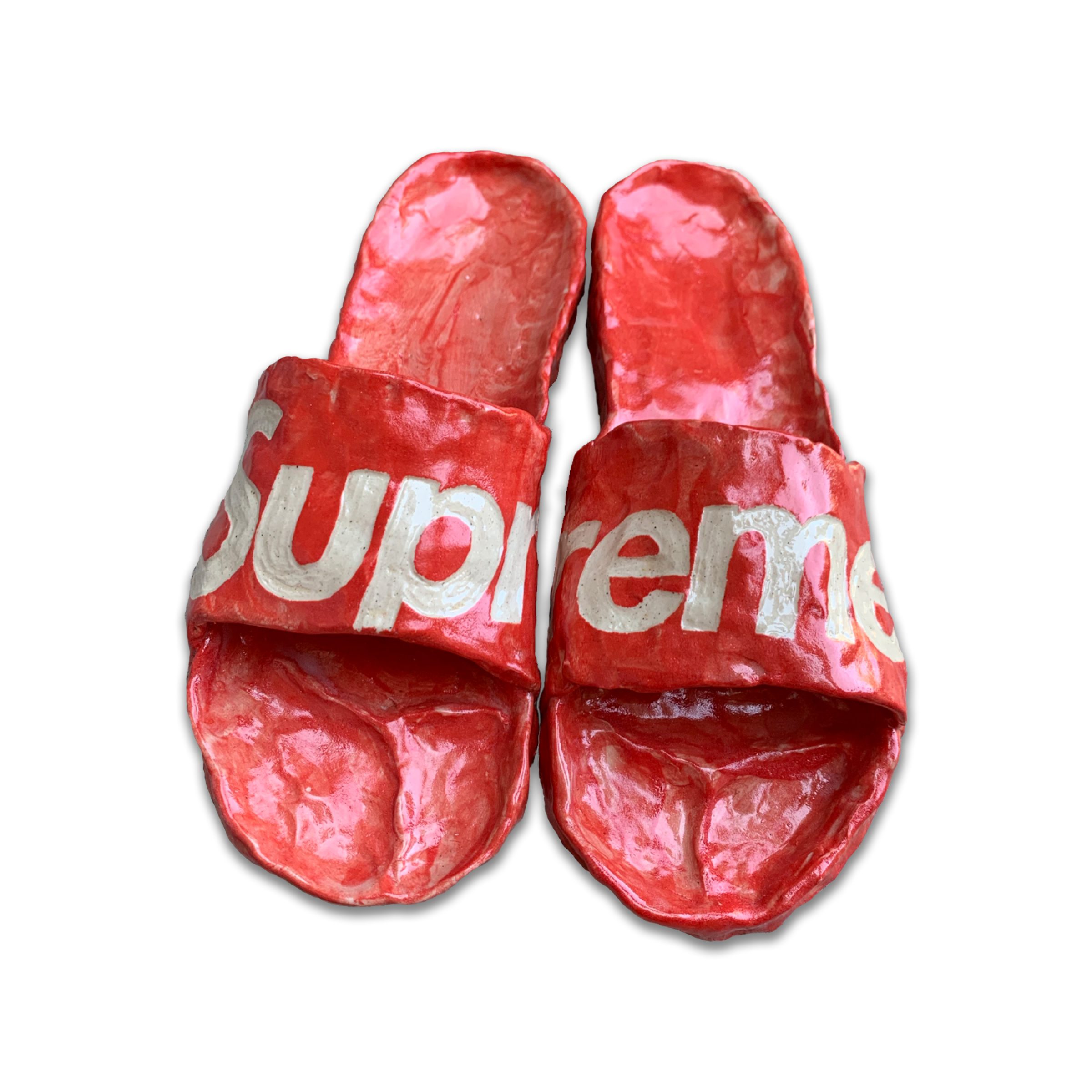 Pair of red slip-on slides with white text across the straps, crafted from clay with a glossy glazed finish. The shoes are positioned side-by-side against a white background, showing wear and texture across their molded surface.