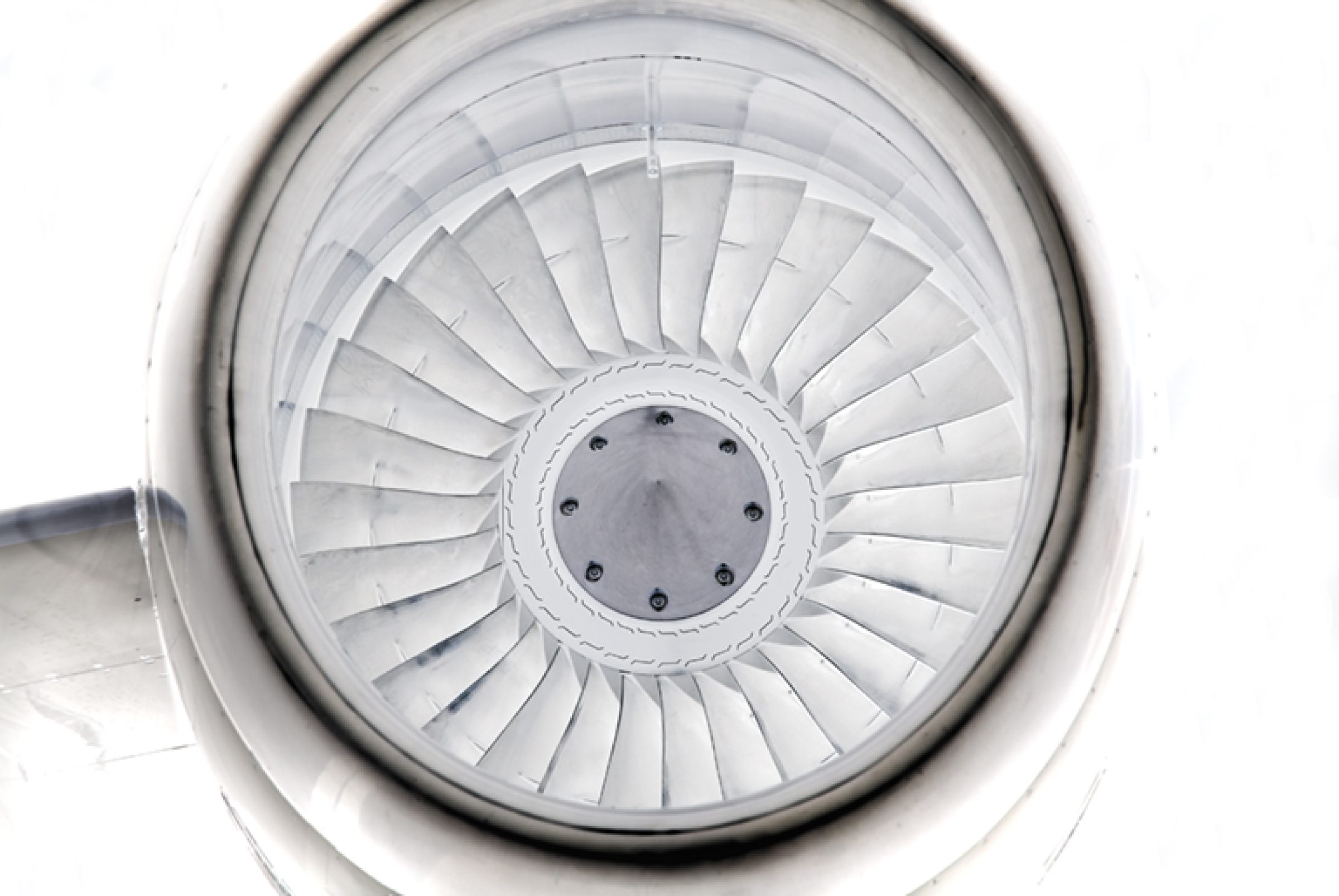 Overhead view of a jet engine's fan blades radiating outward in concentric white metal rings, photographed from directly above. The geometric pattern creates a symmetrical spiral composition with a central circular hub, rendered in grayscale tones.