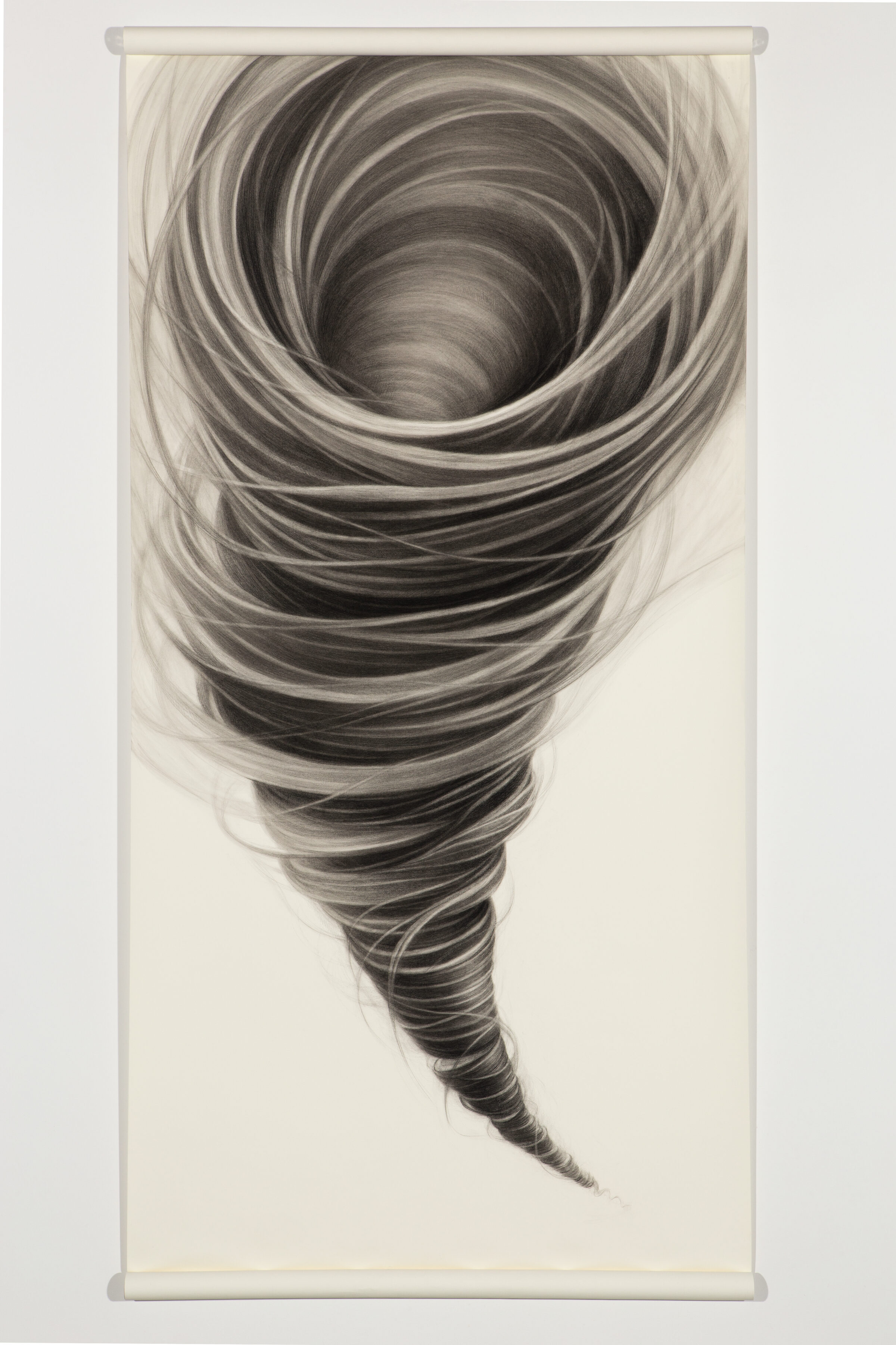 A dramatic spiral composition rendered in charcoal depicts a tornado viewed from above, with concentric swirling lines that gradually darken toward the center void. The tightly wound bands of gray and black create a hypnotic sense of motion and depth against the pale paper ground.