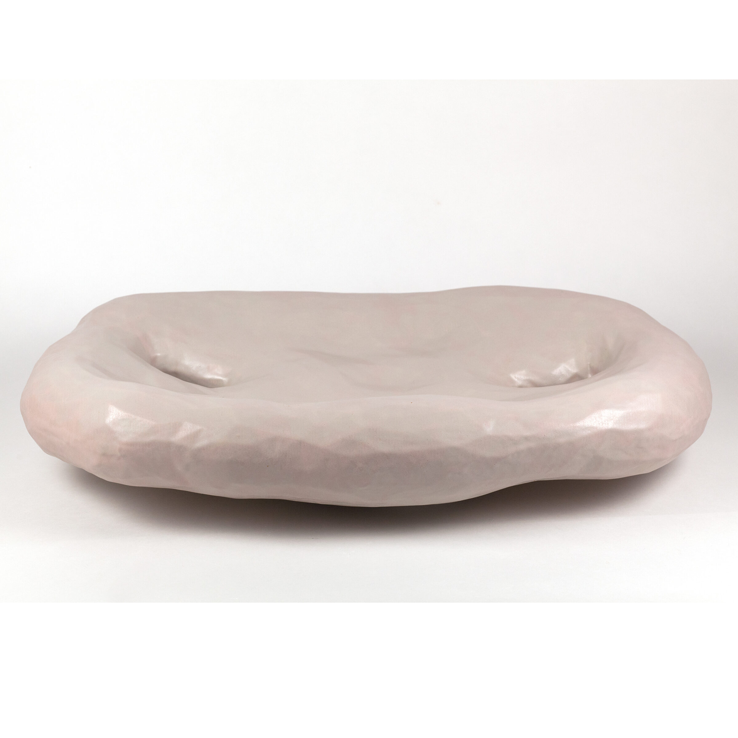 A pale pink ceramic bowl with an organic, elongated form featuring two shallow indentations across its curved surface, finished with a subtle gloss glaze.