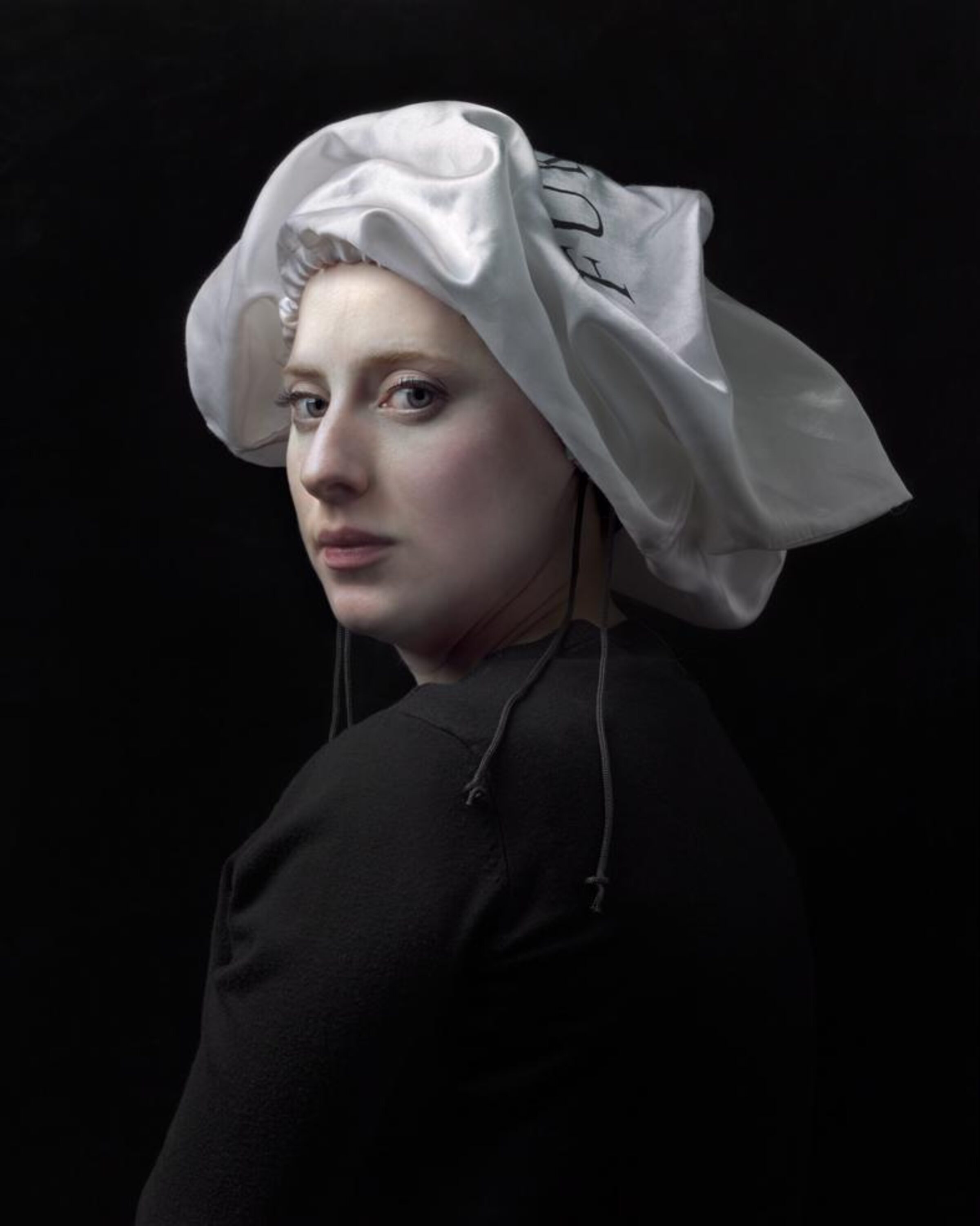 Portrait of a figure shown in three-quarter view against a black background, wearing a black garment with a distinctive white linen headwrap with voluminous folds. The figure gazes toward the viewer with a composed expression, rendered in a highly detailed, photorealistic style with naturalistic skin tones and subtle modeling of light and shadow.