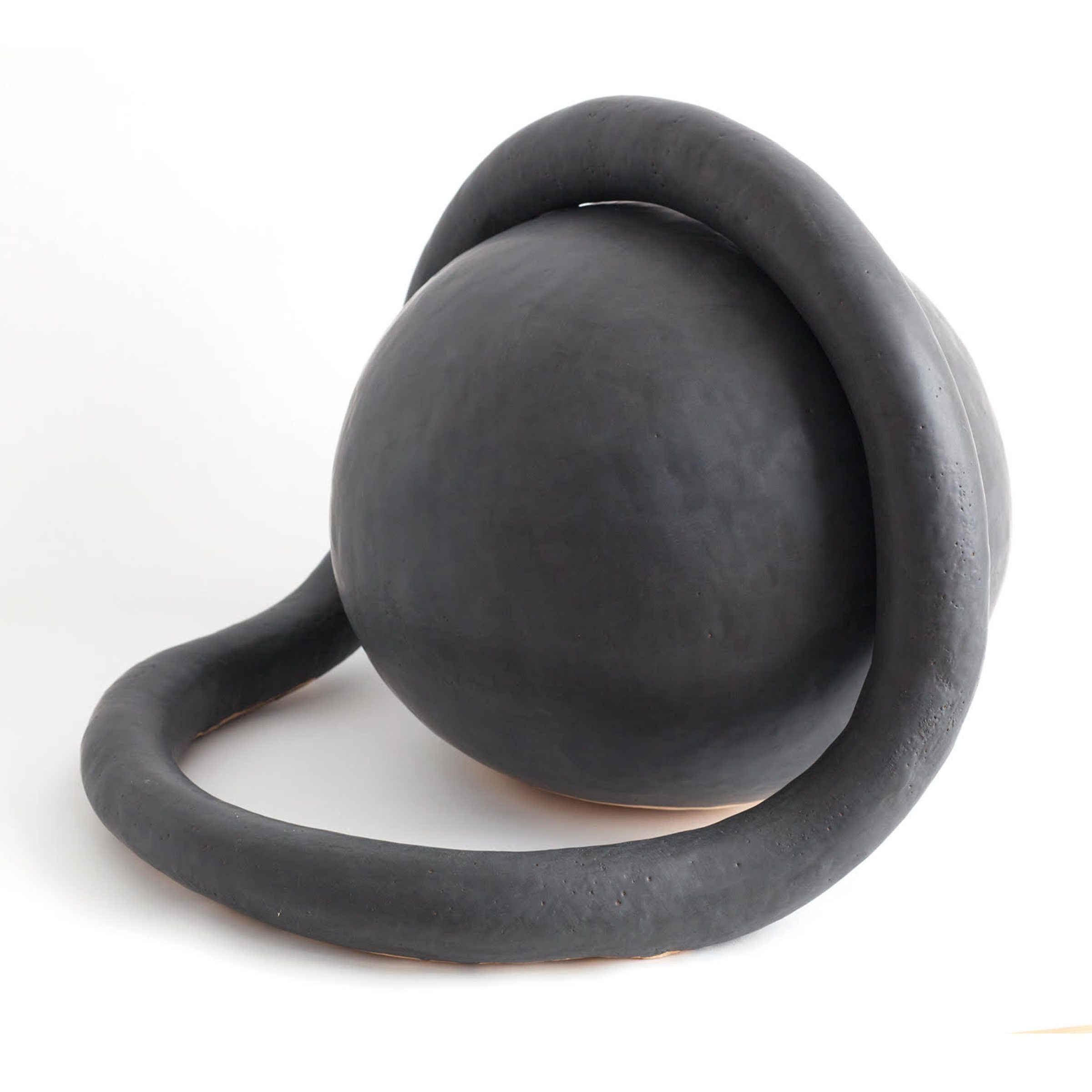 Abstract ceramic sculpture in dark charcoal glaze featuring a curved, organic form with a spherical element perched atop a sweeping, loop-like base, set against a white background.
