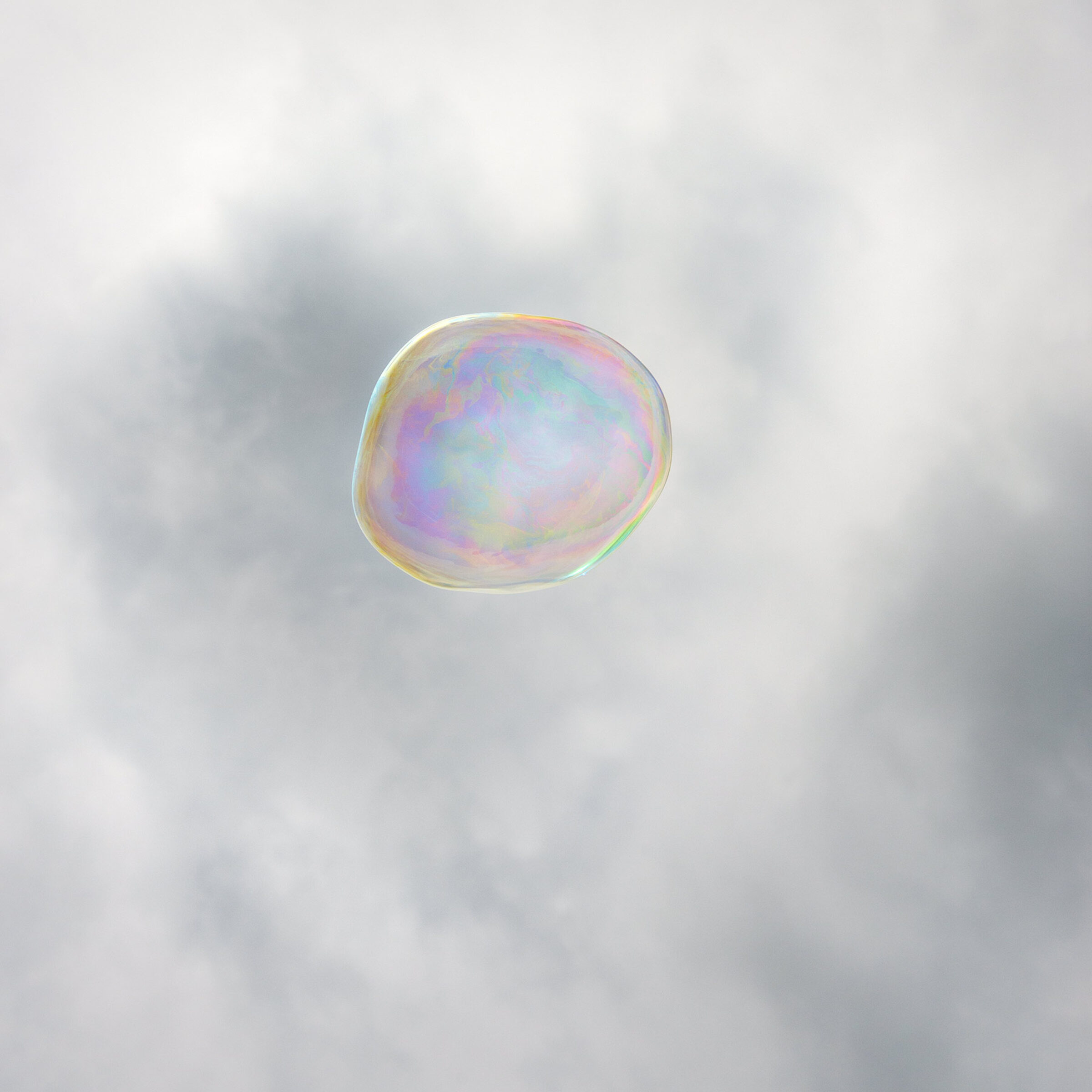 A translucent soap bubble floats against a soft, clouded gray sky. Iridescent pastel hues—pink, blue, yellow, and green—shimmer across its delicate spherical surface, creating an ethereal and luminous effect.
