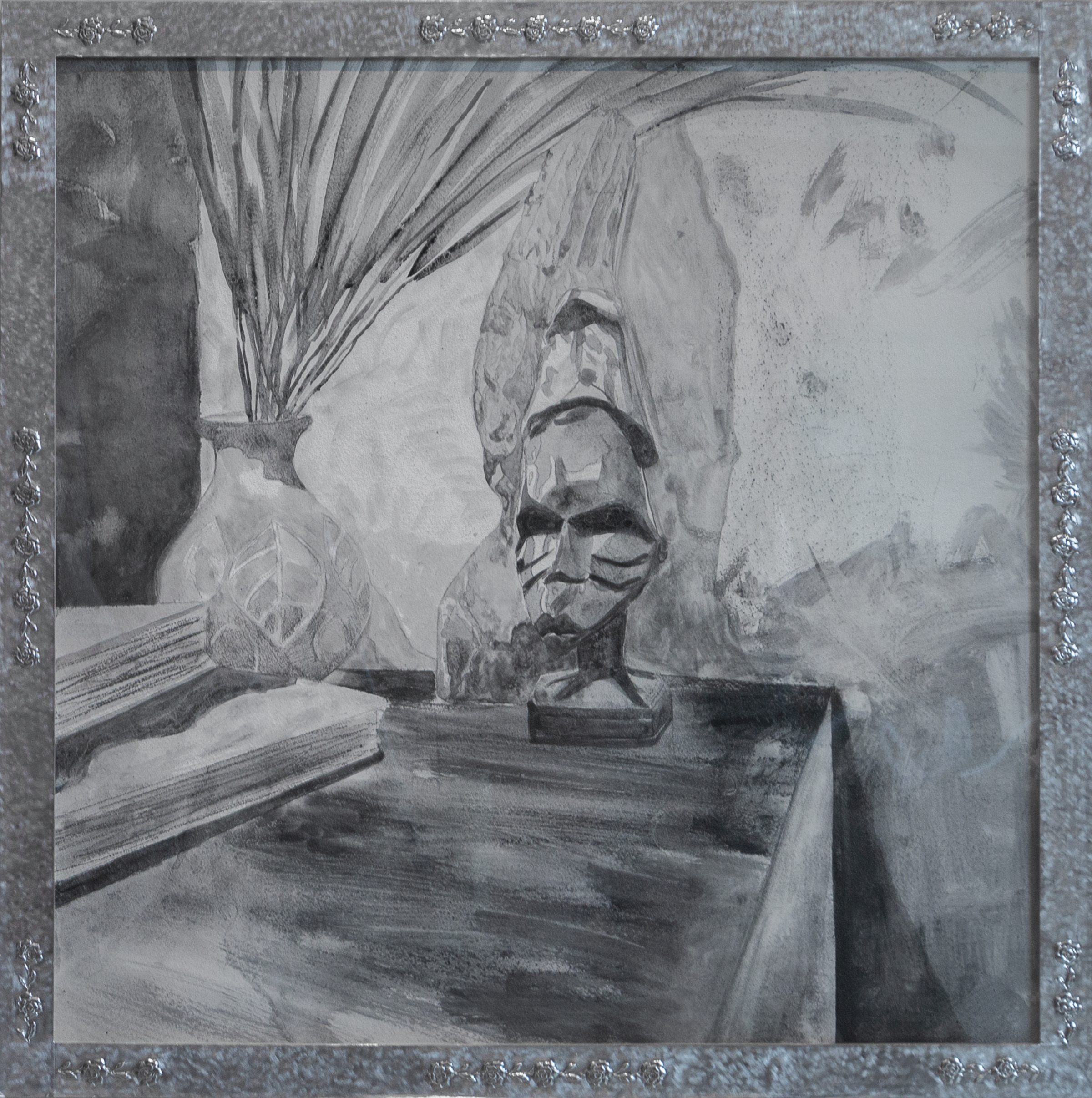 A graphite drawing on gesso depicting a sculptural bust with pronounced facial features and a contemplative expression, positioned on a wooden surface. Dried palm fronds in a decorative vessel are visible to the left, while atmospheric marks and gestural strokes create depth in the background. The work is presented in an ornate silvered frame.