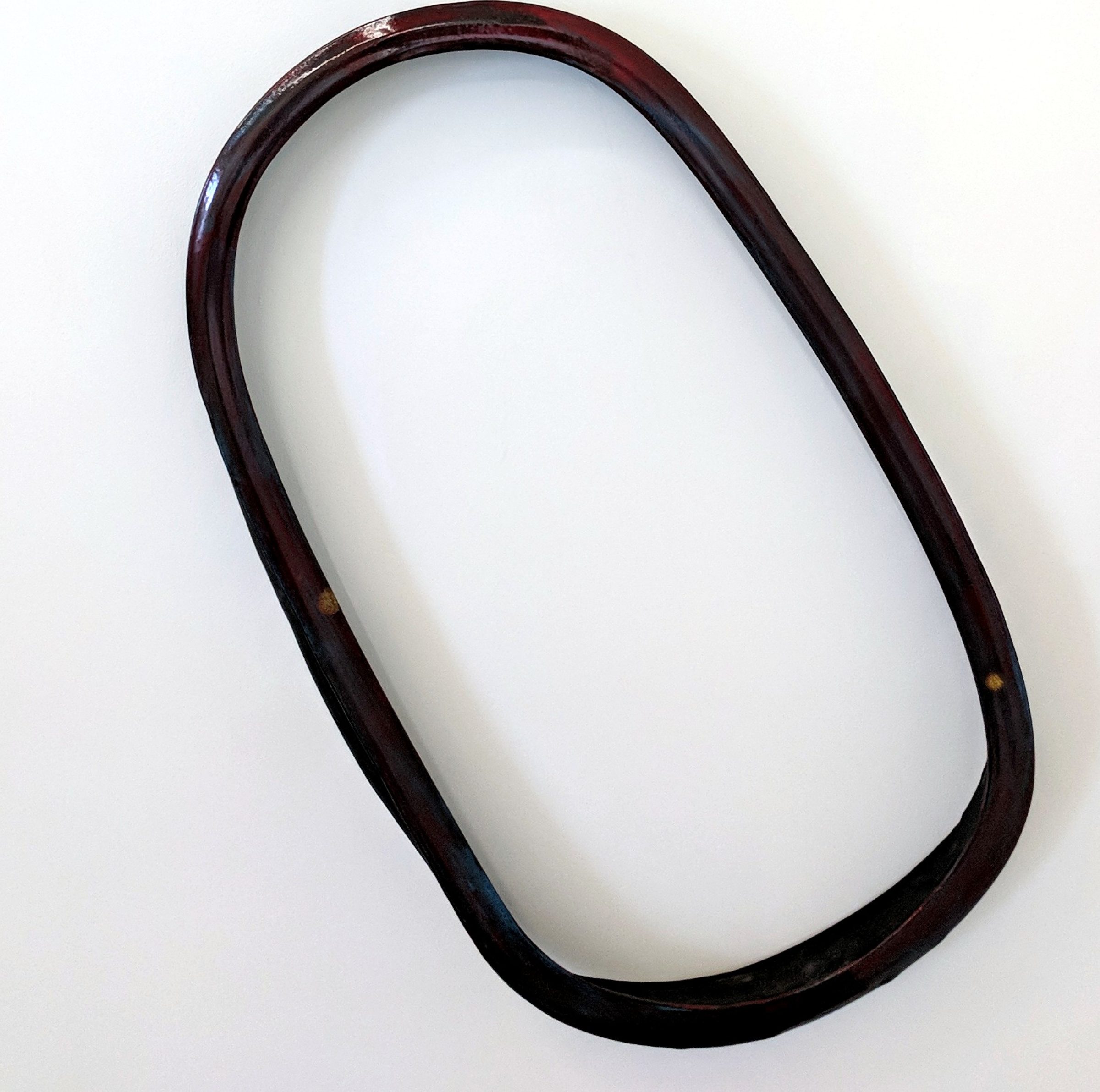A dark reddish-brown ceramic ring with a smooth, curved form sits against a white background. The sculptural object has an organic, minimalist aesthetic with subtle variations in tone and a polished surface.