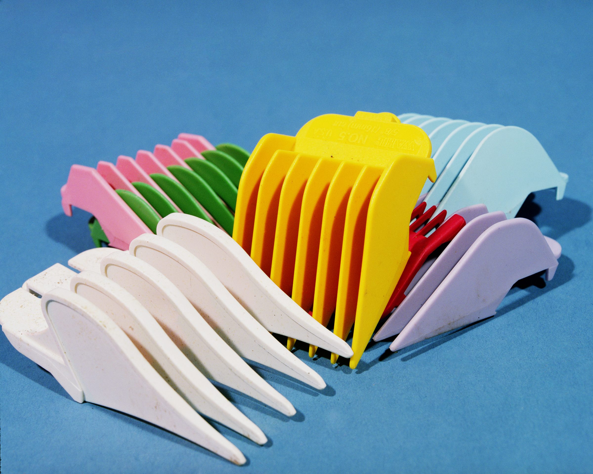 Colorful plastic hair clips arranged in overlapping rows against a bright blue background, displaying shades of white, pink, green, yellow, red, light blue, and purple in a playful still-life composition.