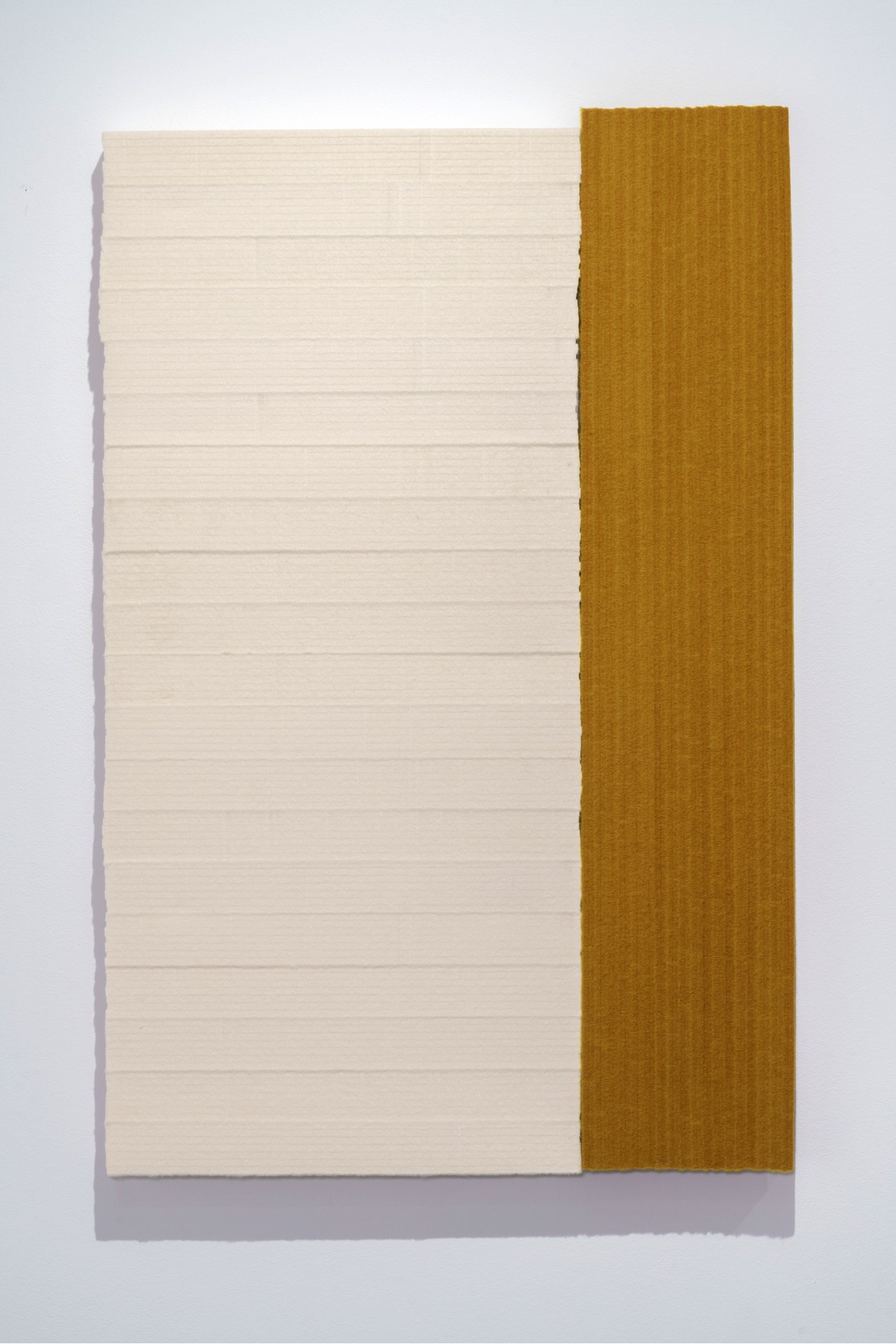 Two panels of industrial felt mounted on plywood: a cream-colored panel with horizontal striations on the left, adjoining a warm ochre panel on the right. The rectangular composition is set against a light background, casting a subtle shadow.