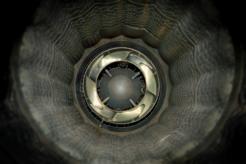A symmetrical view down a cylindrical tunnel with concentric ribbed walls in gray and black tones, centered on a metallic circular aperture with reflective surfaces and a dark spherical core.