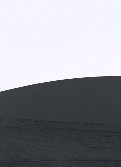 Minimalist composition dividing the frame horizontally into a pale upper section and dark lower half, with a curved horizon line suggesting an abstract landscape or geological formation. Subtle tonal gradations and soft focus create a contemplative, atmospheric quality.