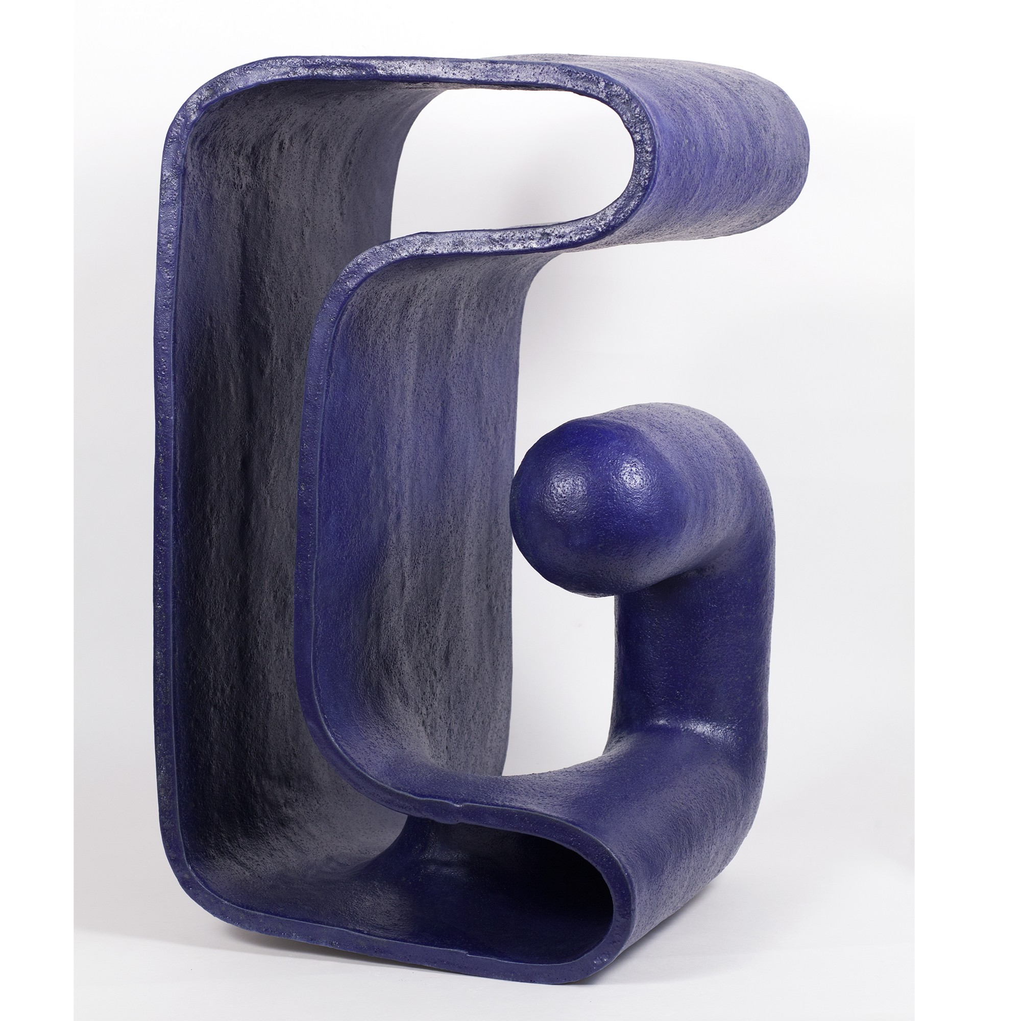 A deep blue ceramic sculpture with a glossy glaze featuring an abstract, organic form that resembles a stylized finger or curved gesture. The piece has smooth, rounded surfaces with hollow sections and a bulbous protrusion, creating a dynamic three-dimensional composition against a white background.