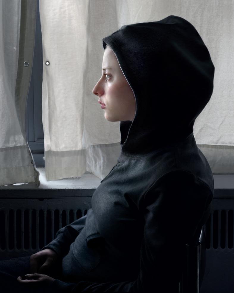 A figure in profile wearing a black hooded garment sits by a window with sheer white curtains. The minimalist composition features soft natural light against neutral tones and a dark radiator below the window sill.