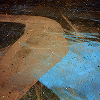 Abstract composition featuring organic, flowing forms in earth tones—rust, brown, and tan—contrasting sharply with a vivid turquoise blue section. The layered, textured surface suggests accumulated materials or weathered surfaces, creating depth through overlapping planes and varied tonal gradations.
