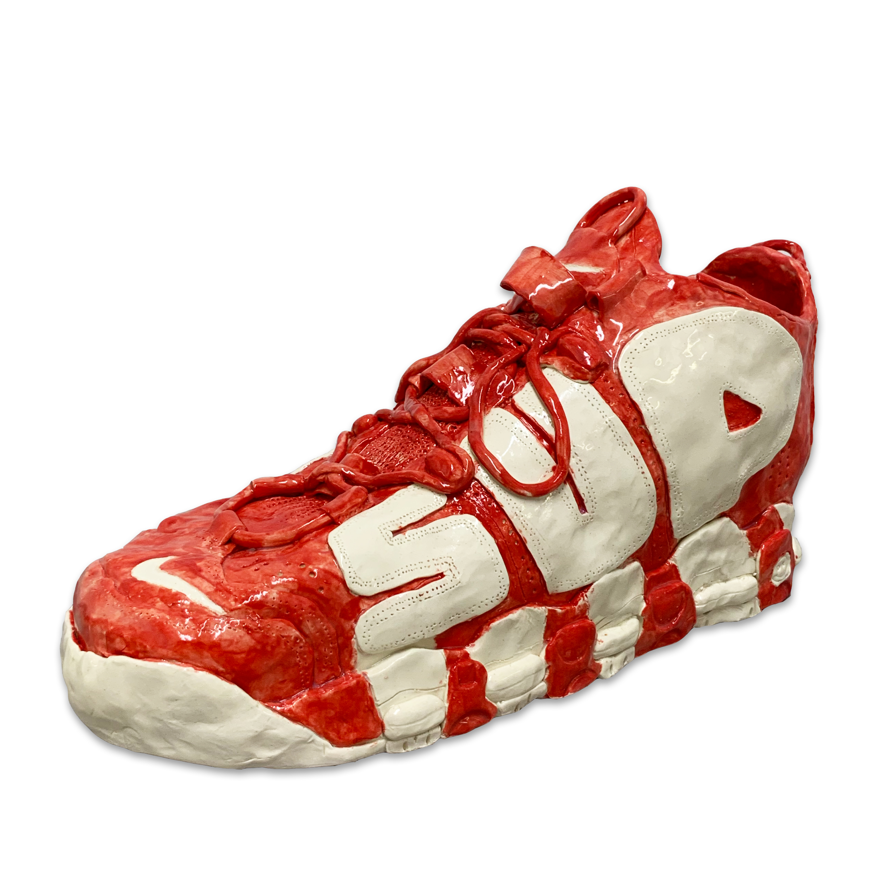 A sculptural sneaker rendered in bright red and cream-colored clay with a glossy glazed finish. The shoe features exaggerated proportions with a bulbous silhouette, prominent sole detailing, and an oversized lace system, presented against a white background.