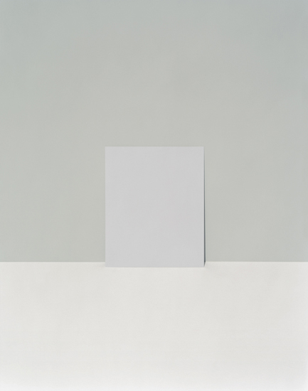 A minimalist composition featuring a white rectangular form standing vertically against a soft gray wall, casting a subtle shadow. The work employs a restrained palette of grays and whites with precise geometric forms, emphasizing negative space and the quiet interplay of light and shadow.