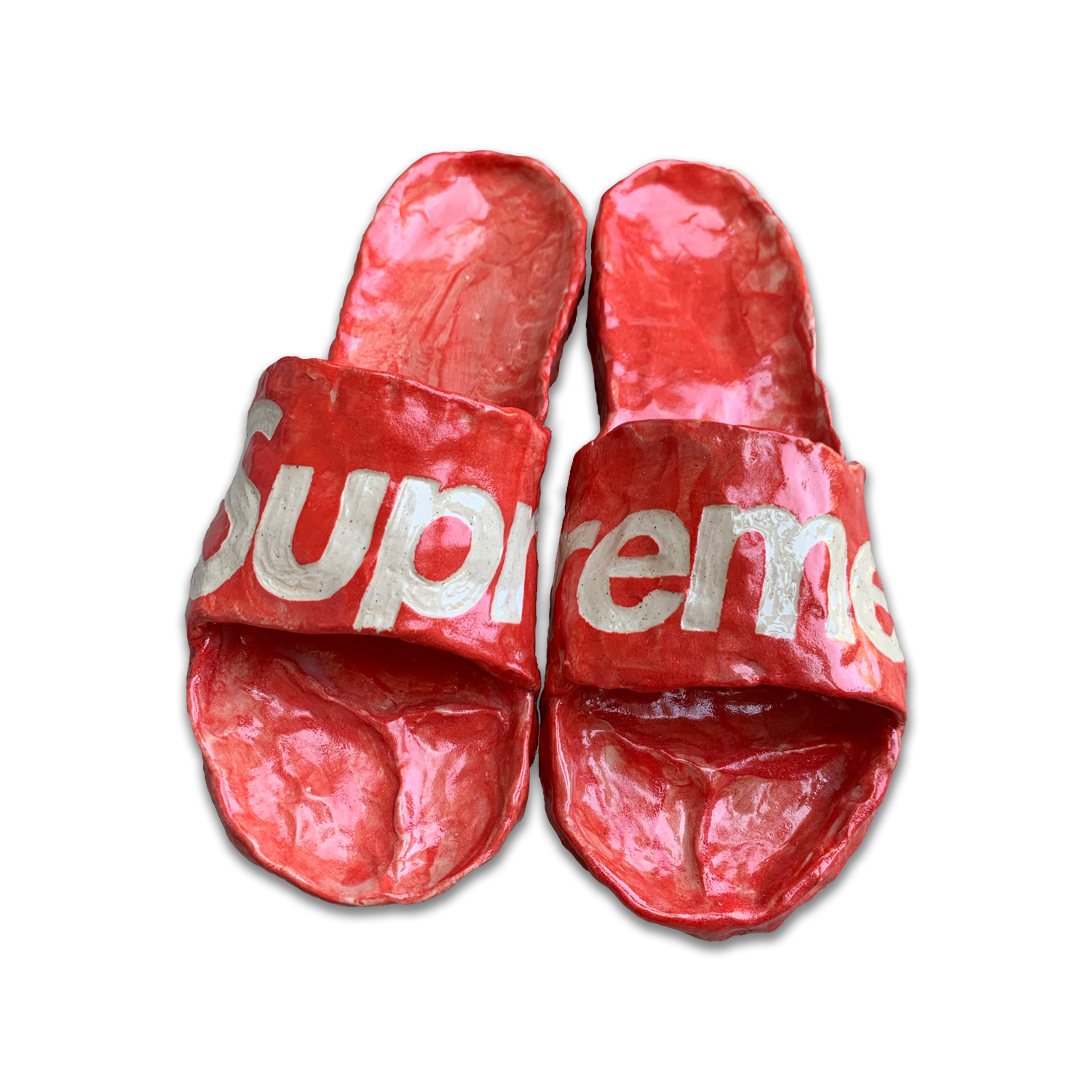 Pair of red slip-on slides with white text across the straps, crafted from clay with a glossy glazed finish. The shoes are positioned side-by-side against a white background, showing wear and texture across their molded surface.
