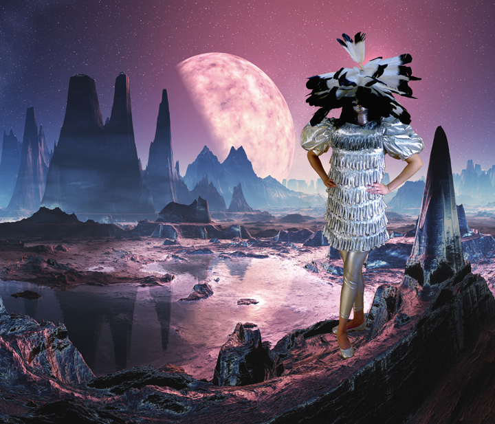 A surreal figure in a fringed white garment stands on a rocky alien landscape, their head replaced by a mass of black silhouettes of birds in flight. Behind them, a massive glowing pink moon rises above towering rock formations beneath a purple and blue starlit sky, while the terrain below glows in shades of mauve and rose.