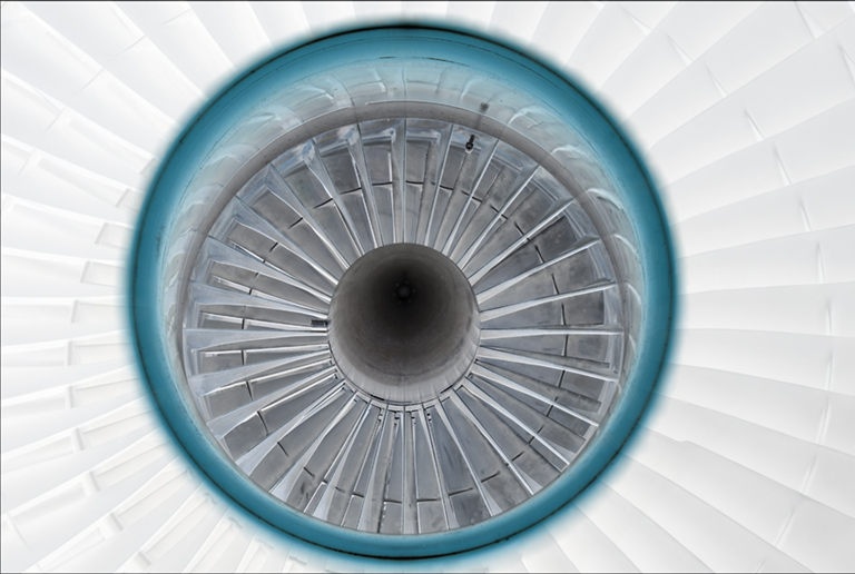 Symmetrical overhead view of a jet engine intake, featuring concentric rings of metal blades radiating from a dark central core, framed by a turquoise outer ring against a pale geometric background.