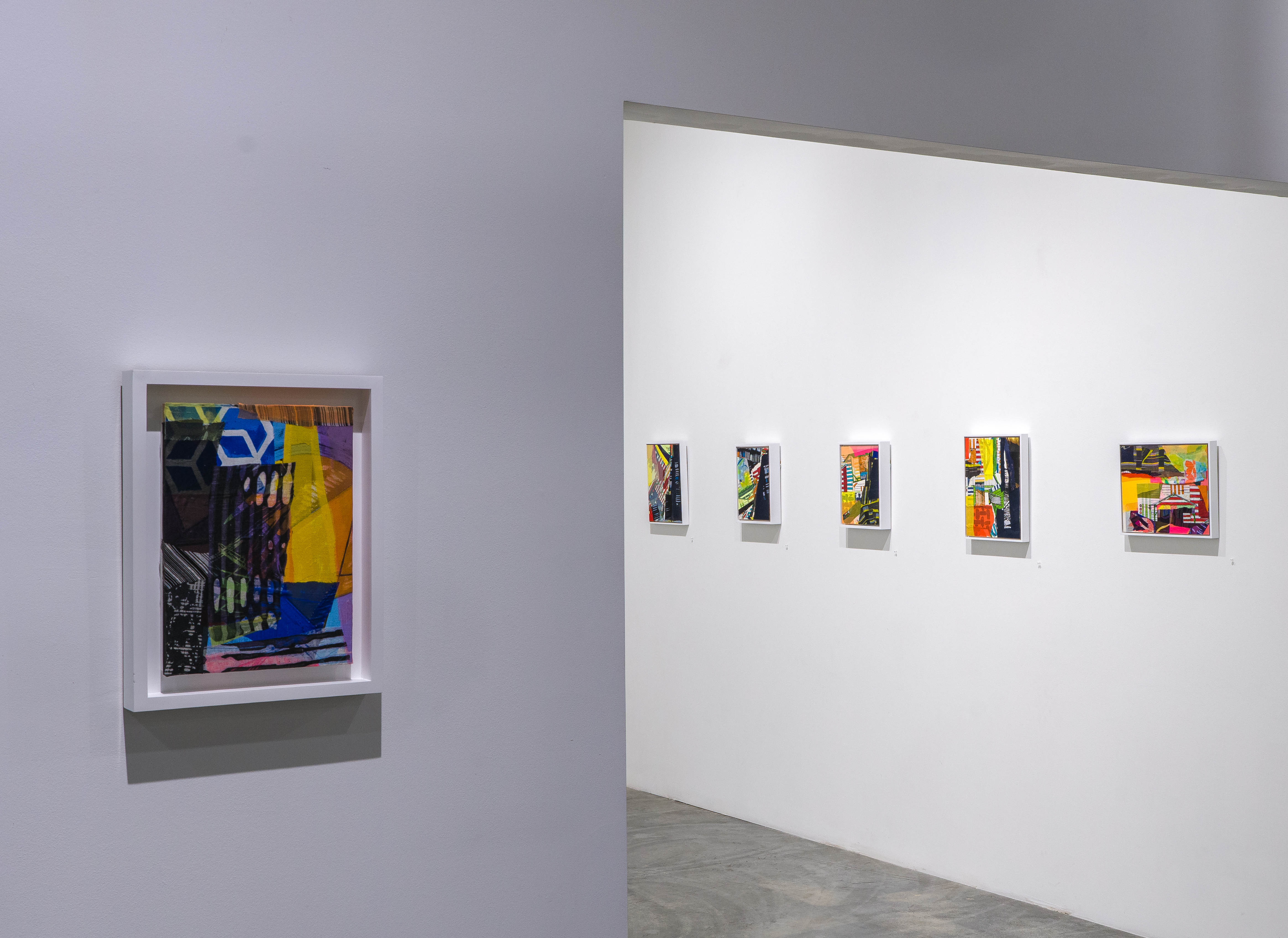 Gallery view showing a large colorful abstract mixed-media work mounted on the left wall featuring layered geometric shapes in blue, yellow, black, and pink, alongside five smaller framed works displayed in a row on the right wall, each with vibrant abstract compositions in bold color palettes.