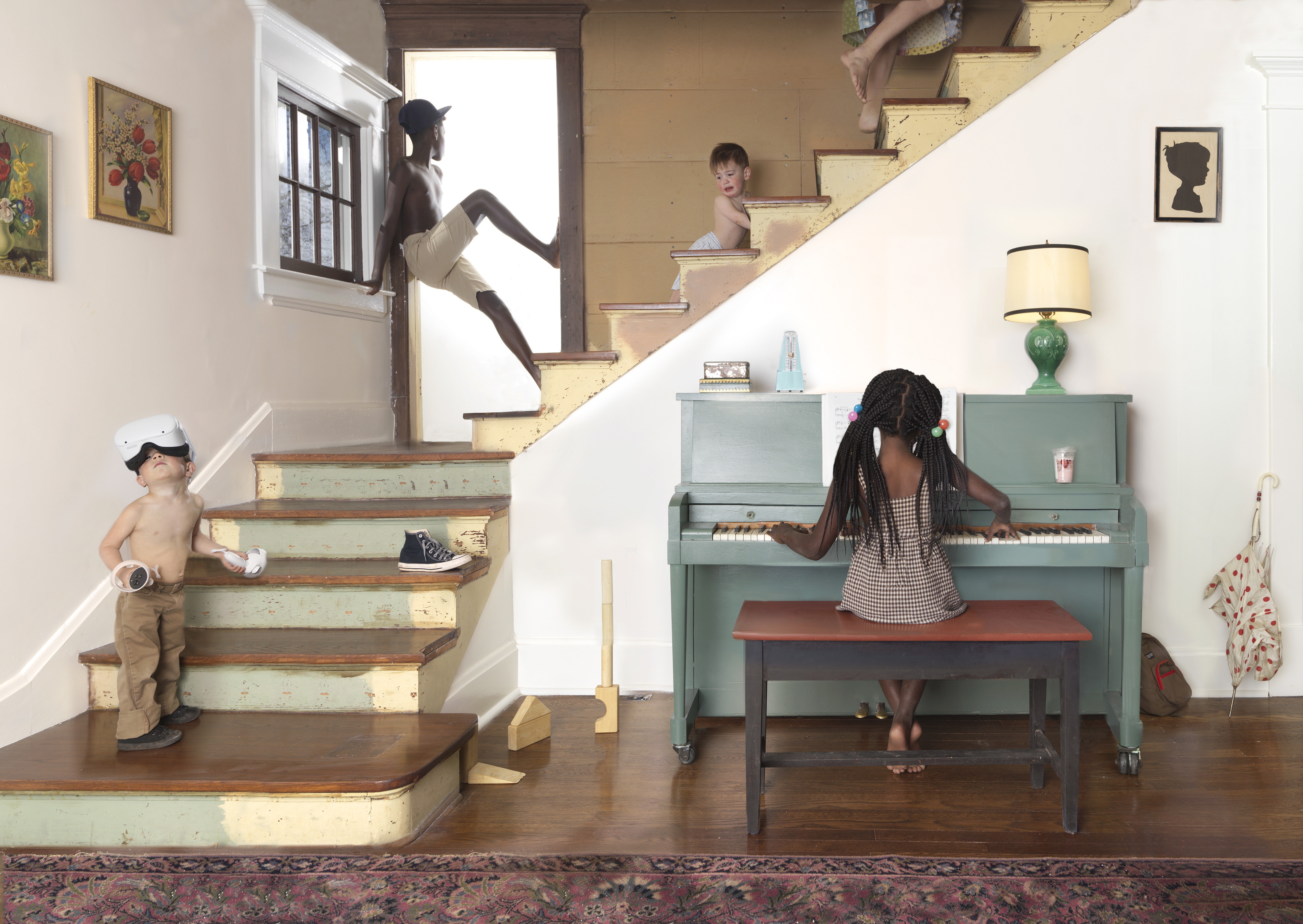 A staged domestic interior scene featuring multiple Black children and young people engaged in various activities throughout a cream-colored room with distressed wooden stairs. A child in a VR headset stands on the lower left, another plays piano at a green upright in the center-right, figures climb and lounge on the staircase, and additional children appear on upper steps and in doorways, creating a playful, surreal composition that layers childhood activities across different levels of the space.