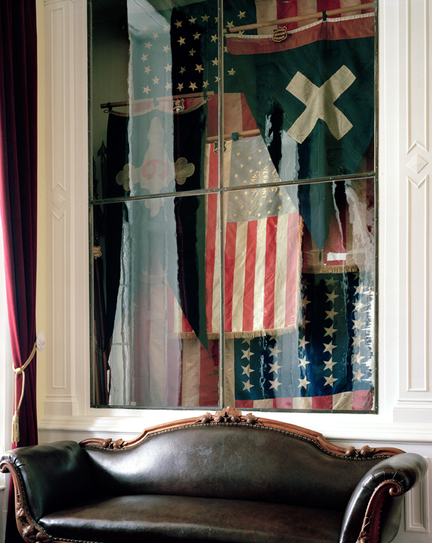 Large-scale inkjet print displayed behind glass featuring overlapping American flags and patriotic imagery in red, white, and blue, with a cream-colored X across the center. The composition includes fragmented flag designs with stars and stripes arranged in a layered, collage-like manner against a dark background.