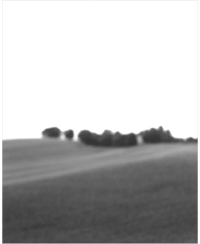 A minimalist black and white landscape featuring a gently rolling field in the foreground with a soft horizon line and distant tree line rendered in soft focus. The composition emphasizes subtle tonal gradations and atmospheric perspective, creating a contemplative, abstract quality.