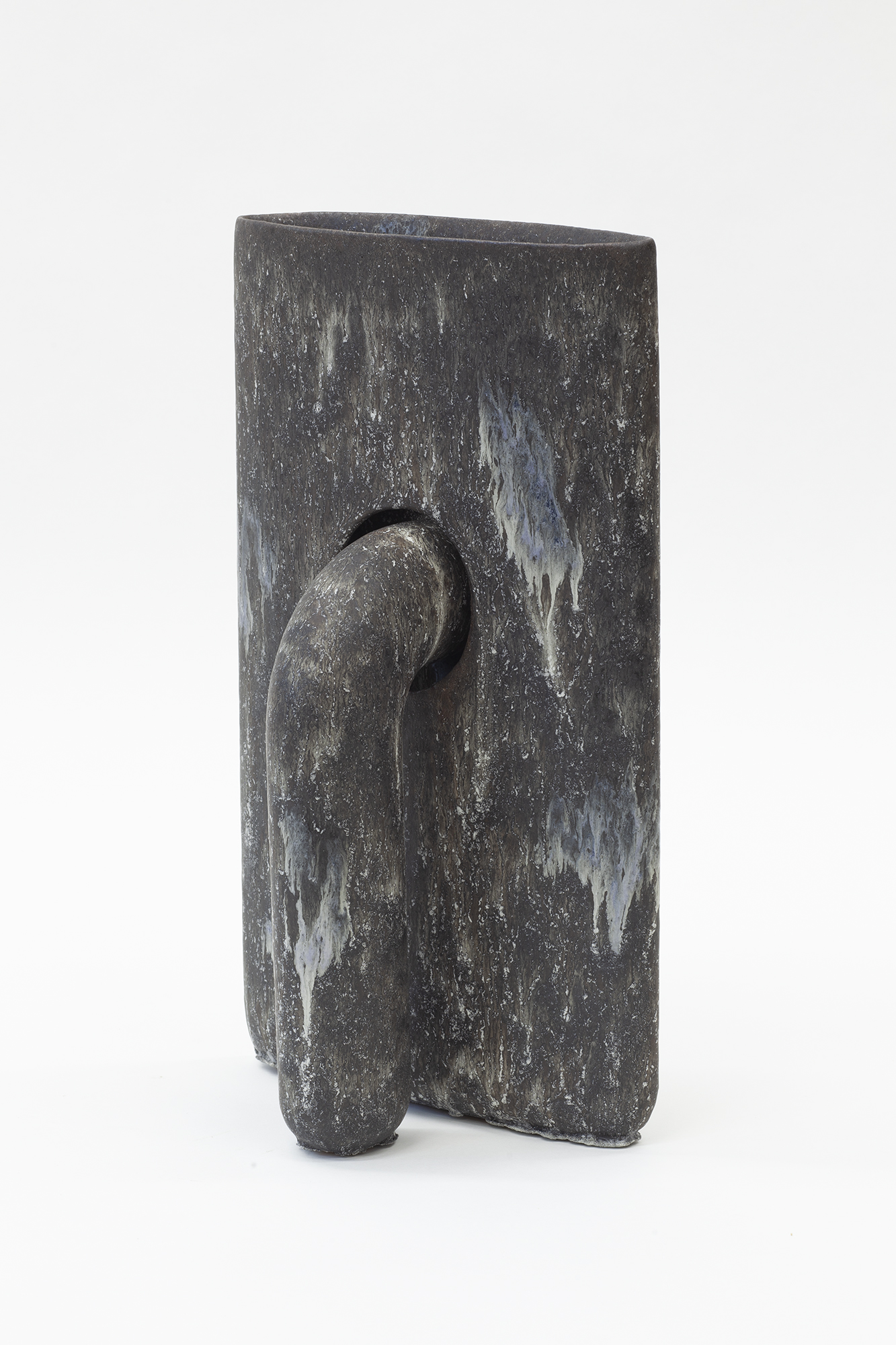Dark gray stoneware vessel with a rectangular body featuring weathered white streaking across its surface. A curved, organic form protrudes from the front, creating an abstract sculptural composition that suggests both natural and figural elements.