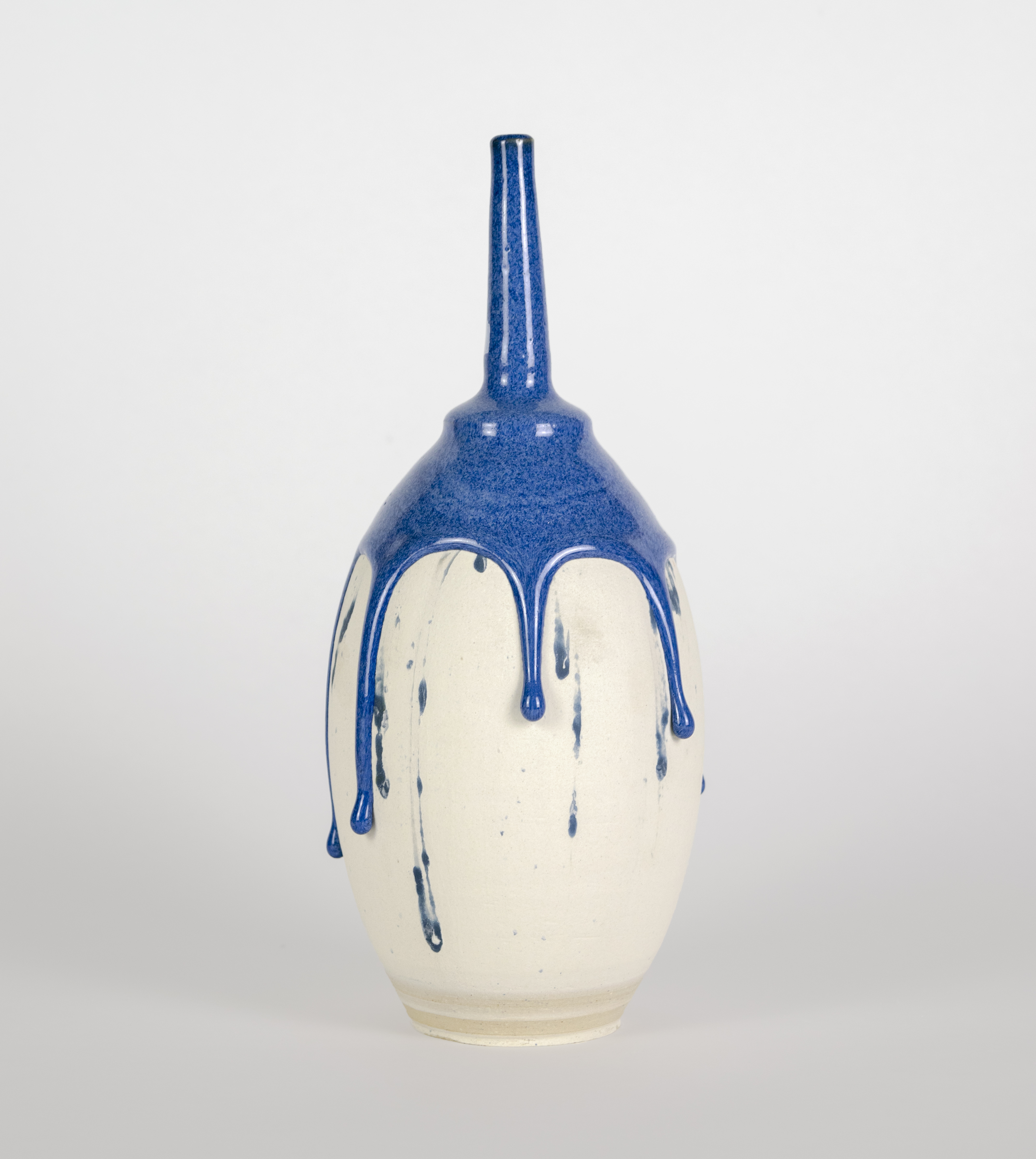 A cream-colored ceramic vessel with a rounded body and tapered neck, finished with a glossy blue glaze on the upper portion that drips downward in organic streaks against the pale surface below.