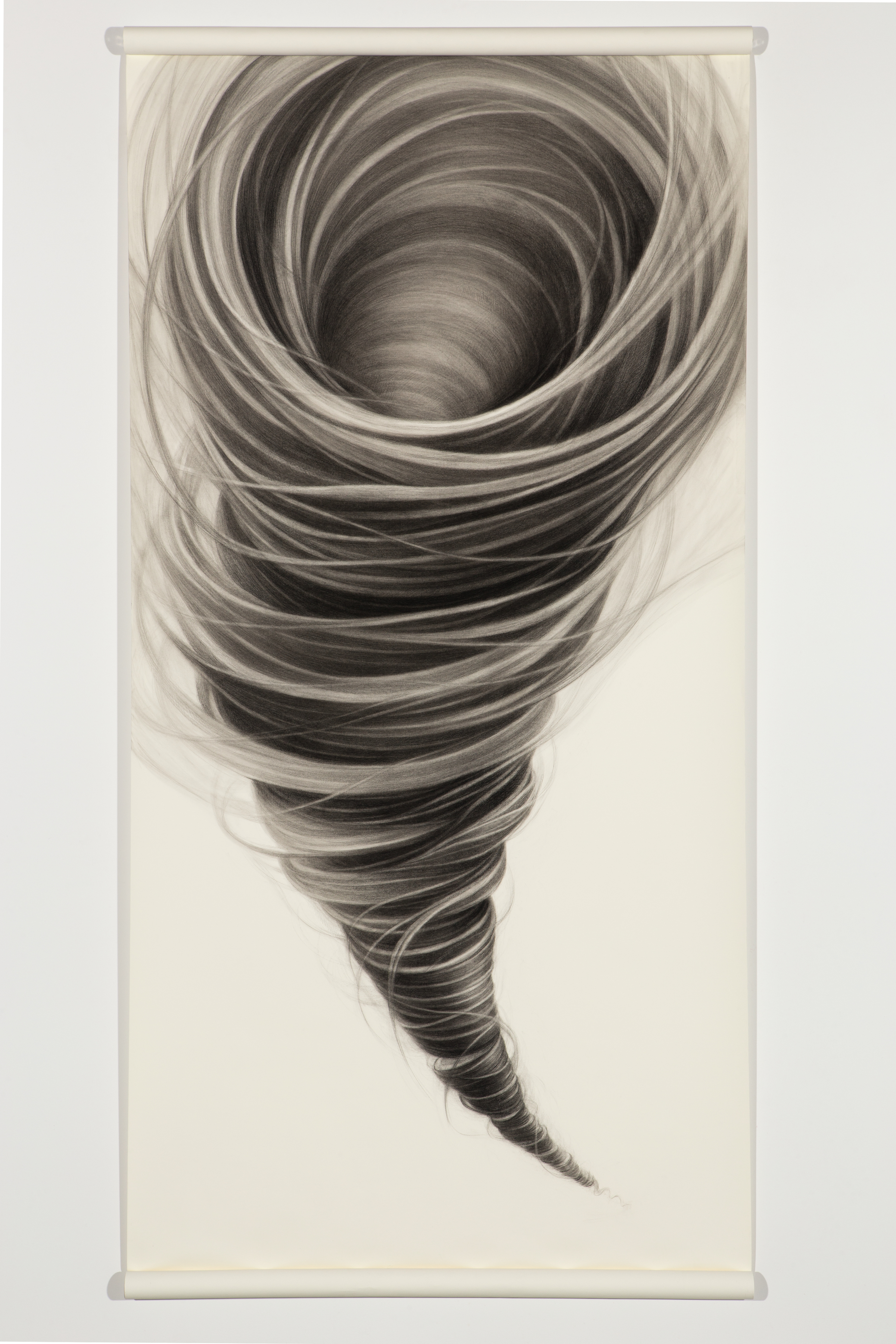 A dramatic spiral composition rendered in charcoal depicts a tornado viewed from above, with concentric swirling lines that gradually darken toward the center void. The tightly wound bands of gray and black create a hypnotic sense of motion and depth against the pale paper ground.