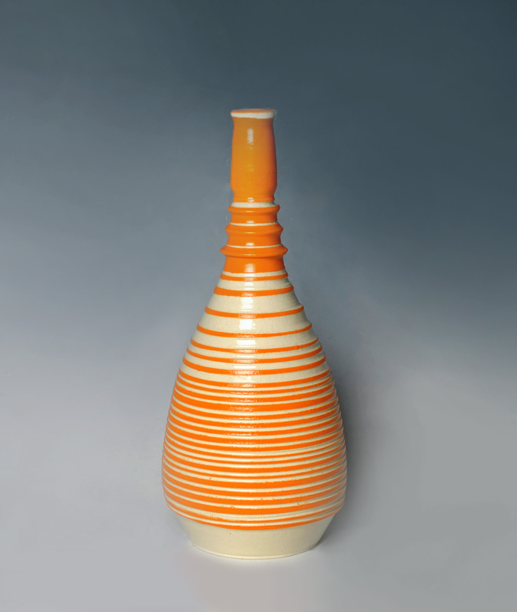 A tall ceramic vessel with a teardrop-shaped body featuring horizontal orange and cream stripes, topped with a narrow cylindrical neck in solid orange glaze against a neutral gray background.
