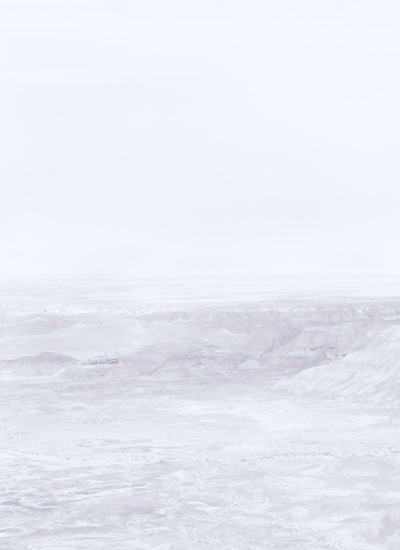 Minimalist landscape featuring layered, undulating terrain in soft whites and grays beneath a pale, overcast sky. The composition emphasizes subtle tonal variations and atmospheric haze across an expansive, largely featureless vista.