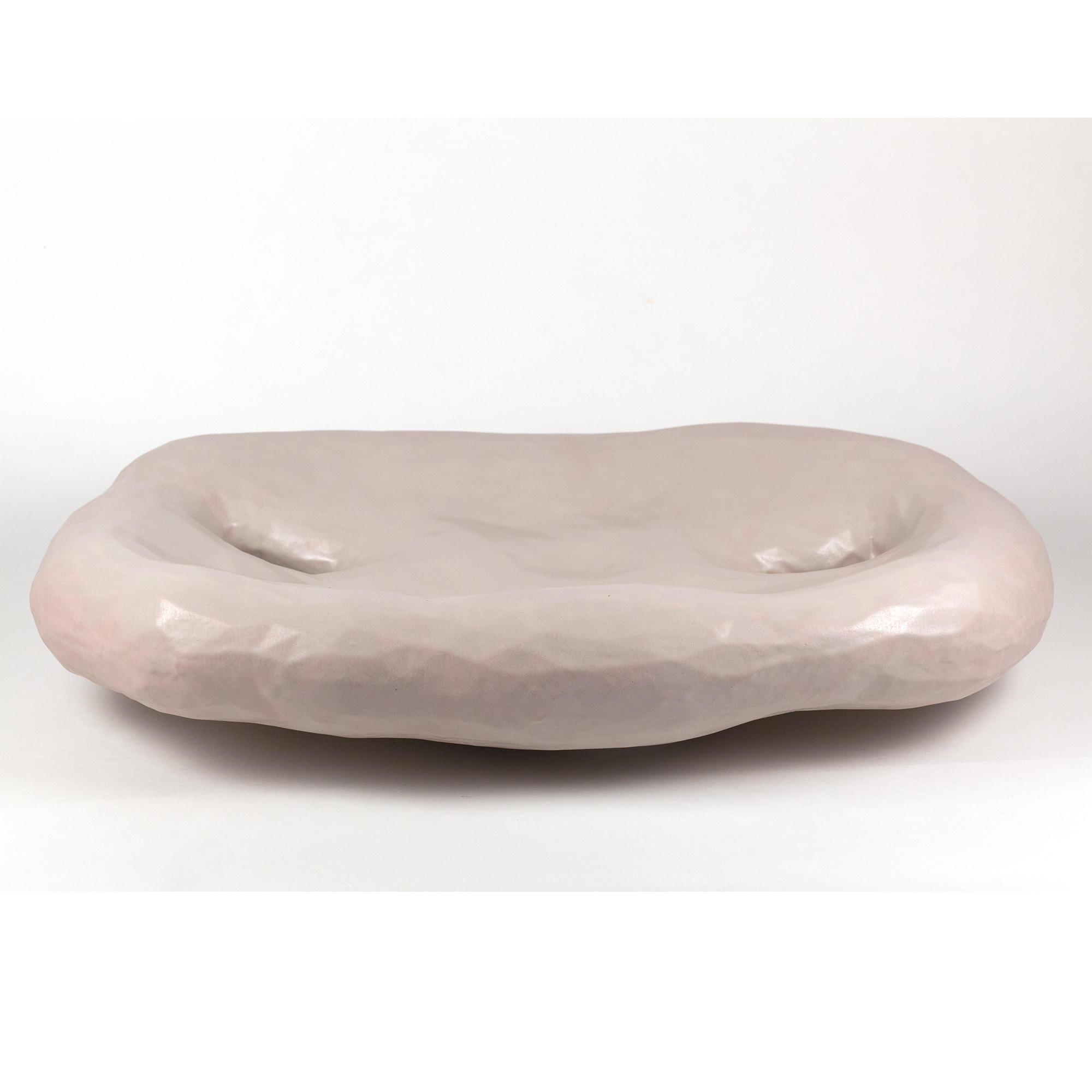 A pale pink ceramic bowl with an organic, elongated form featuring two shallow indentations across its curved surface, finished with a subtle gloss glaze.