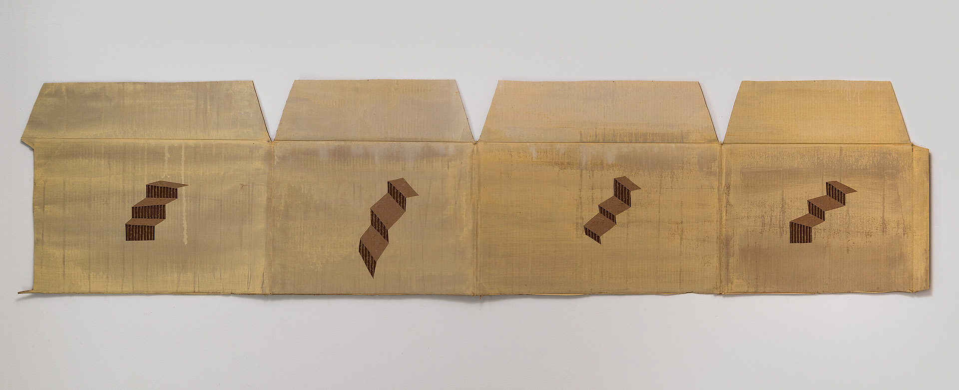 Four connected brass or gold-toned metal panels arranged horizontally, each featuring a cutout pattern of small rectangular forms arranged in a diagonal zigzag configuration, creating negative space that reveals the wall behind.