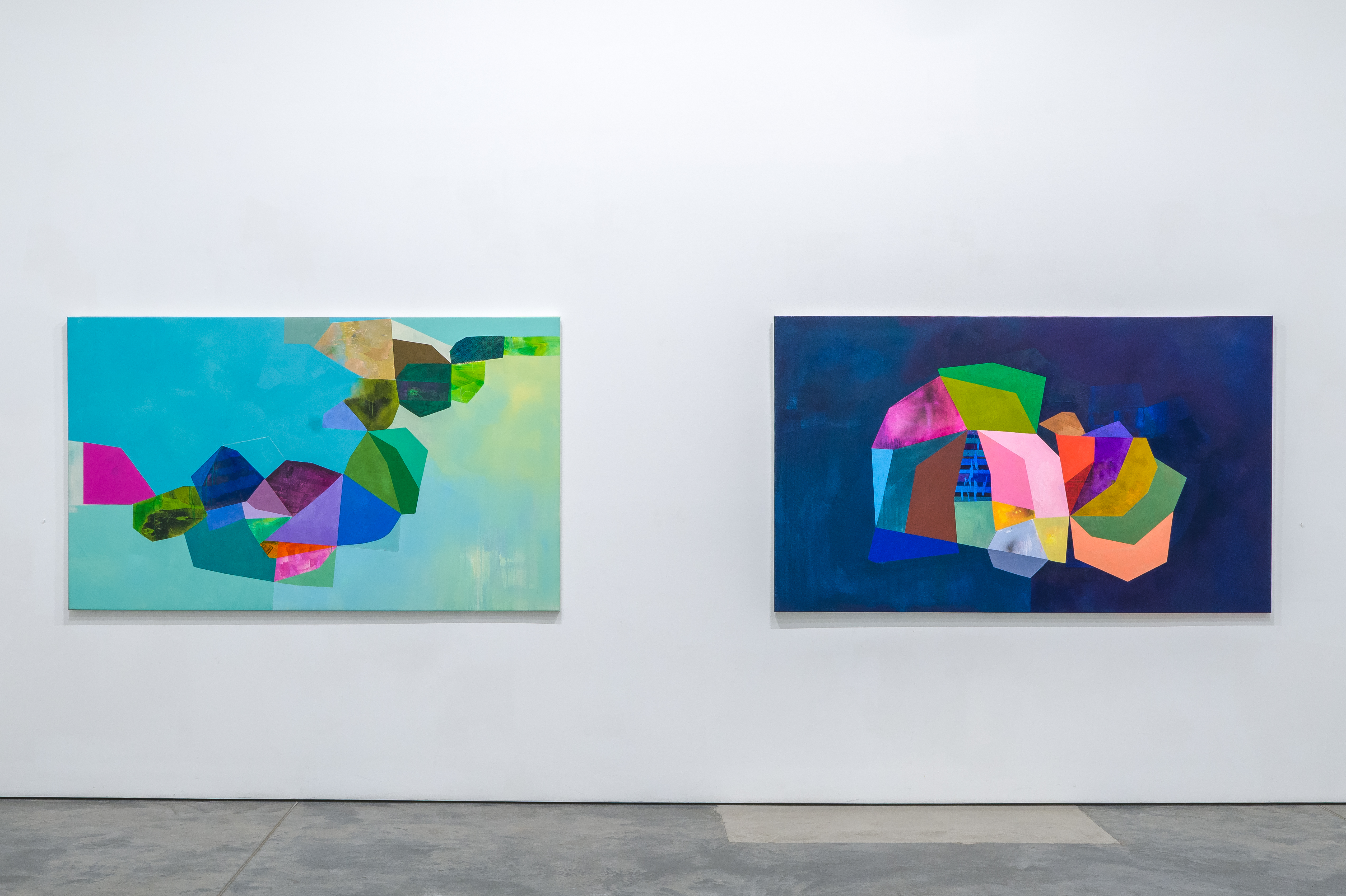 Two large abstract paintings displayed side by side on a gallery wall. The left canvas features a turquoise and pale yellow gradient background layered with overlapping geometric shapes in vibrant magenta, blue, green, and orange. The right canvas presents a deep navy background with a dynamic composition of colorful polygonal forms in pink, yellow, orange, green, and blue, creating a three-dimensional effect. Both works combine collage, acrylic, and oil techniques with bold color exploration and organic mark-making.