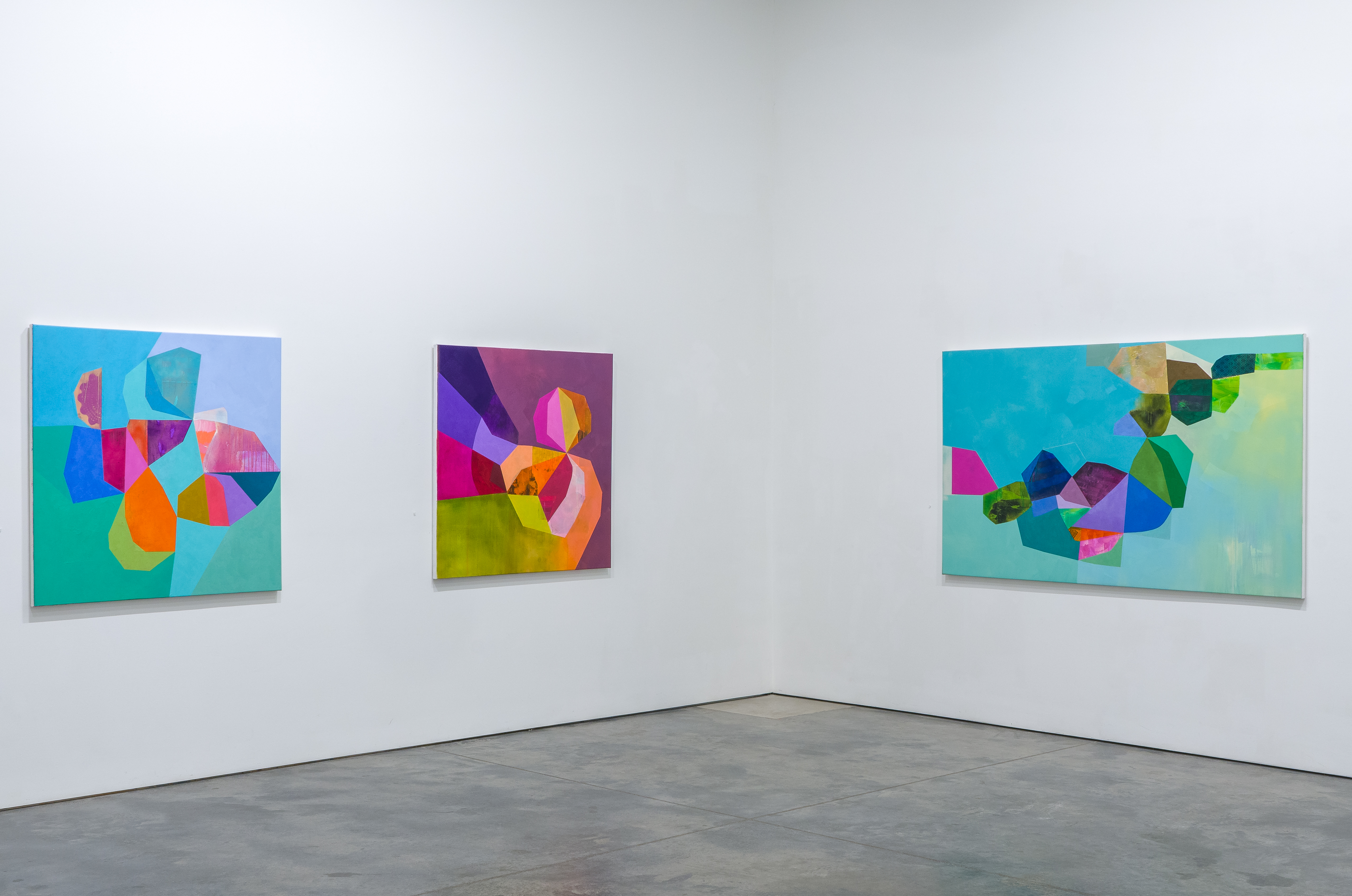Three large abstract paintings with vibrant geometric shapes in shades of turquoise, magenta, orange, yellow, and blue arranged on a white gallery wall. The compositions feature overlapping organic and angular forms created through collage, acrylic, and oil techniques, emphasizing bold color combinations and layered textures.