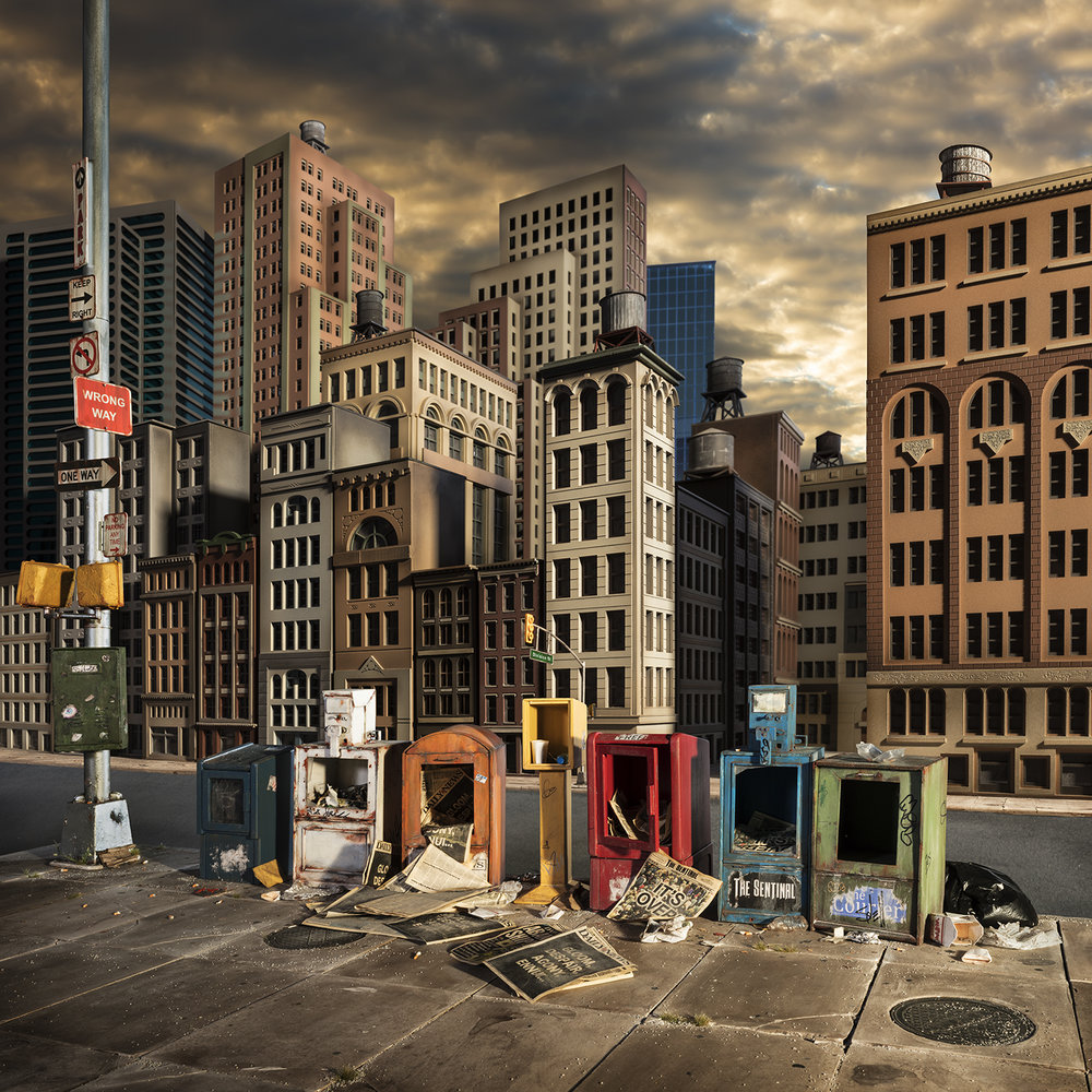 A dystopian urban streetscape dominated by towering brick and stone buildings with water towers on their roofs, beneath a dramatic clouded sky. In the foreground, a row of abandoned, deteriorating newspaper boxes and street furniture in various colors—red, yellow, blue, and green—sit discarded on a concrete sidewalk beside a utility pole with traffic signs, creating a stark contrast between the monumental architecture and the detritus of urban decay.
